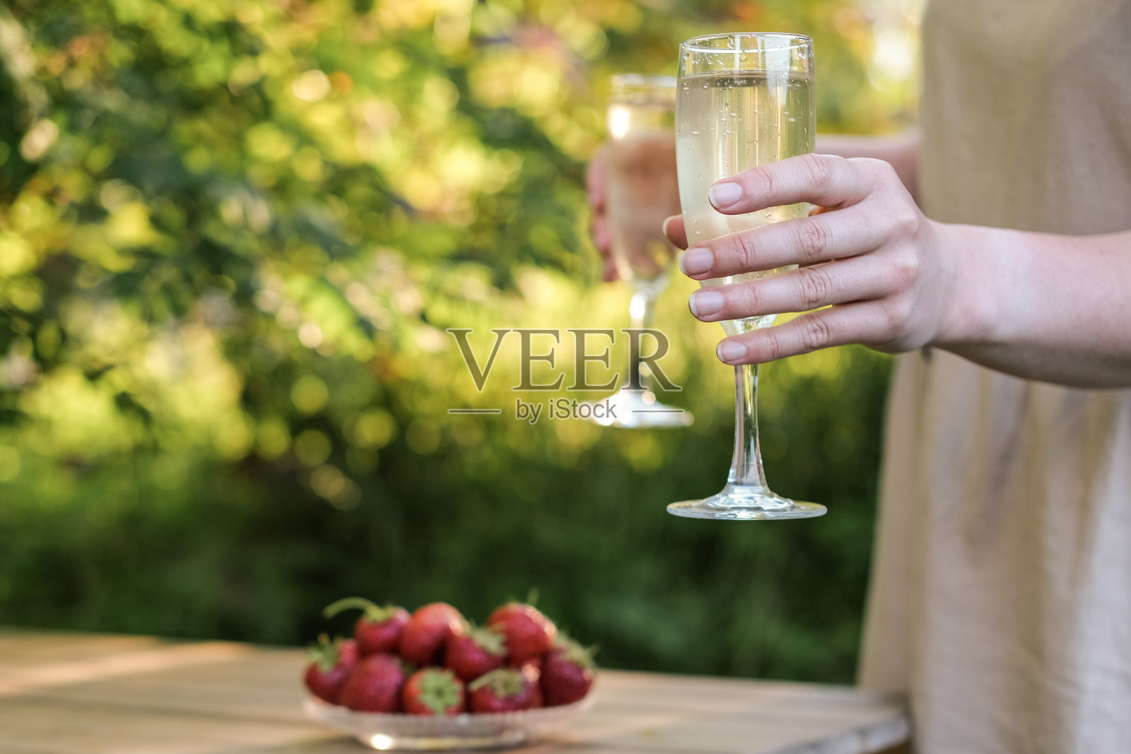 在夏日的花园中，在傍晚的阳光下，女性手中的香槟照片摄影图片