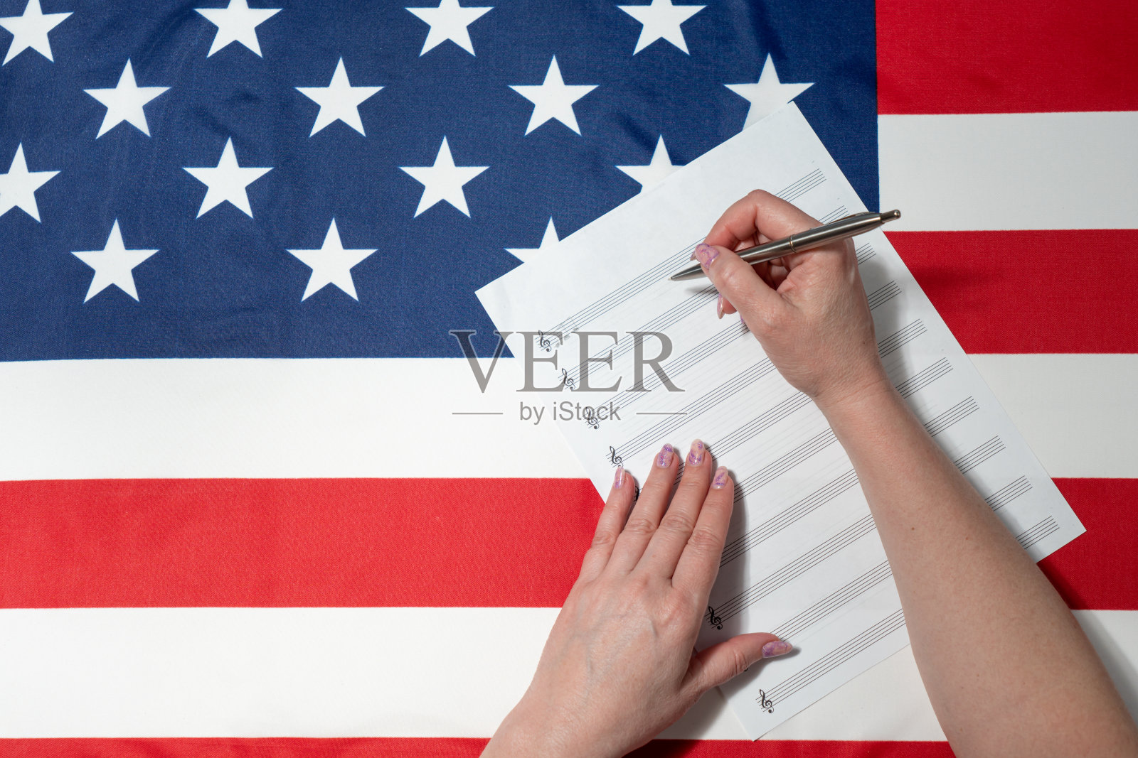 女性的手在乐谱上写音符的特写，背景是美国国旗照片摄影图片