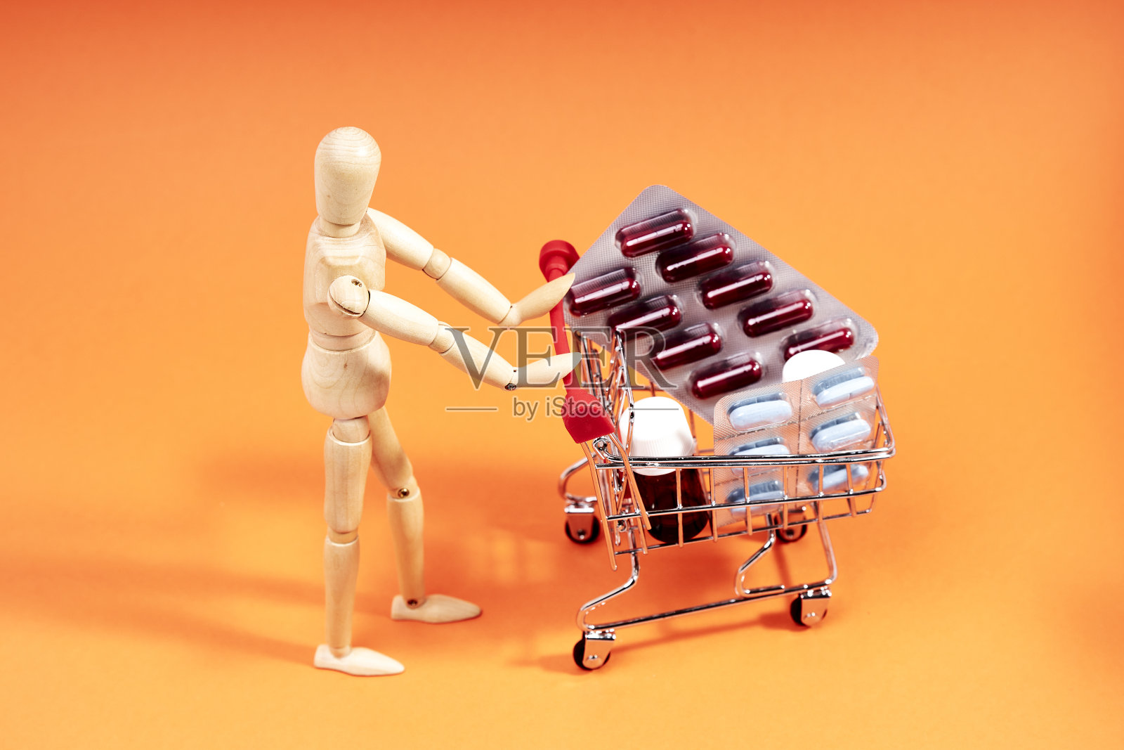假人推着橙色背景的装有药品的购物车。医学的概念照片摄影图片