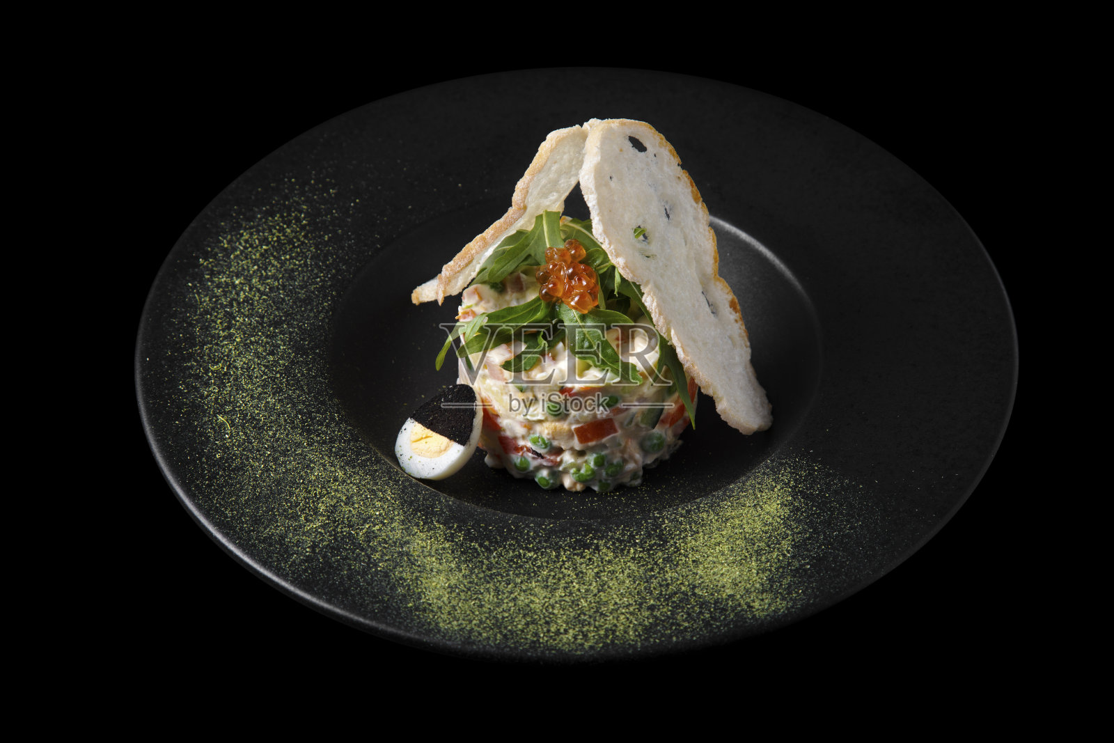 奥利维尔沙拉配芝麻菜、红鱼子酱、胡椒、豌豆、玉米、鸡蛋和面包，装在黑底黑盘子里照片摄影图片