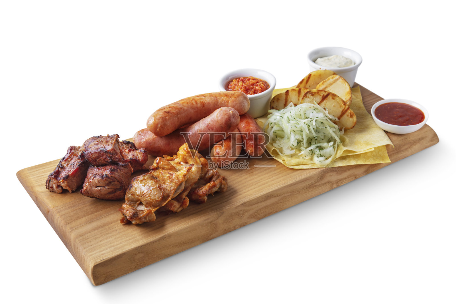 白色背景的板上放着炸香肠、卷心菜、木薯、炸土豆、蘸着不同酱汁的猪肉和鸡肉串照片摄影图片