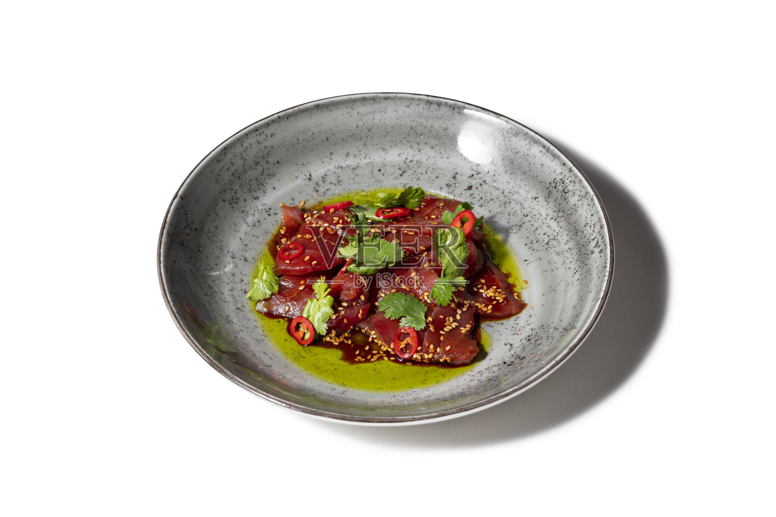 克鲁多金枪鱼配芝麻、香菜叶和切成圈的辣椒。食物放在一个有图案的圆形陶瓷盘子里。这个盘子立在白色的背景上。照片摄影图片