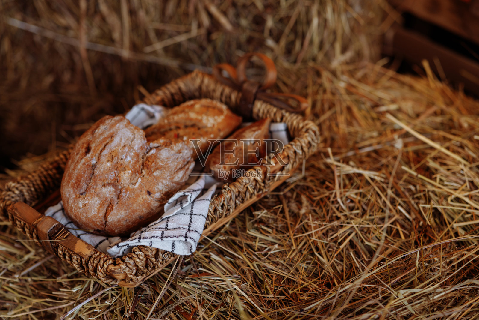 质朴的静物:一个柳条托盘，一块自制的面包放在一卷干草上的桌布上。照片摄影图片