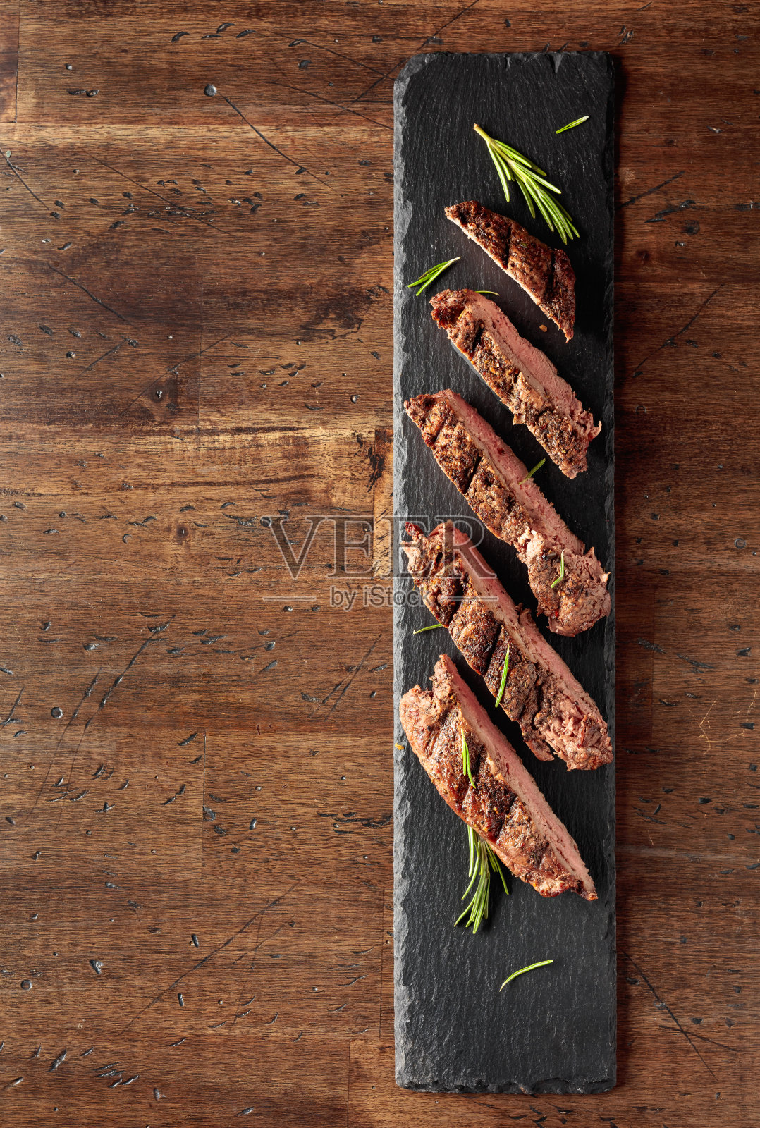 用叉子烤牛排，撒上迷迭香。照片摄影图片