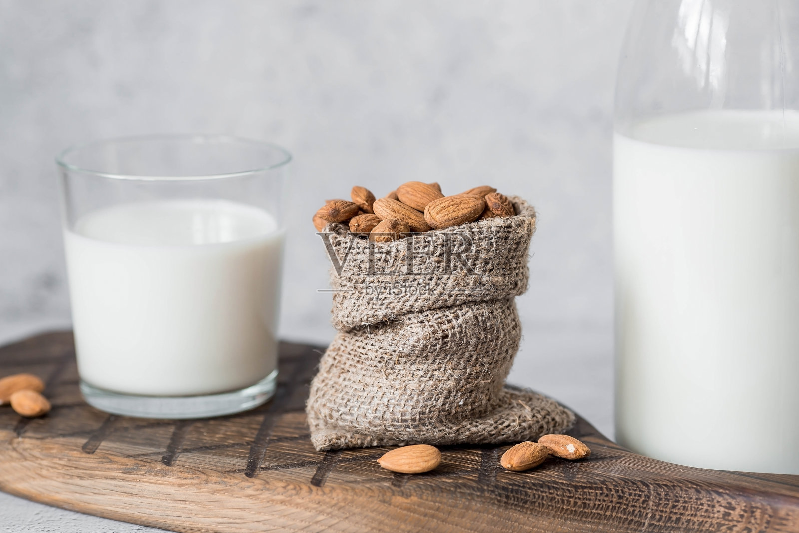 一个玻璃瓶里装着有机杏仁奶，旁边是一个装在袋子里的杏仁，放在石桌上一个时髦的木板上。天然环保产品。照片摄影图片