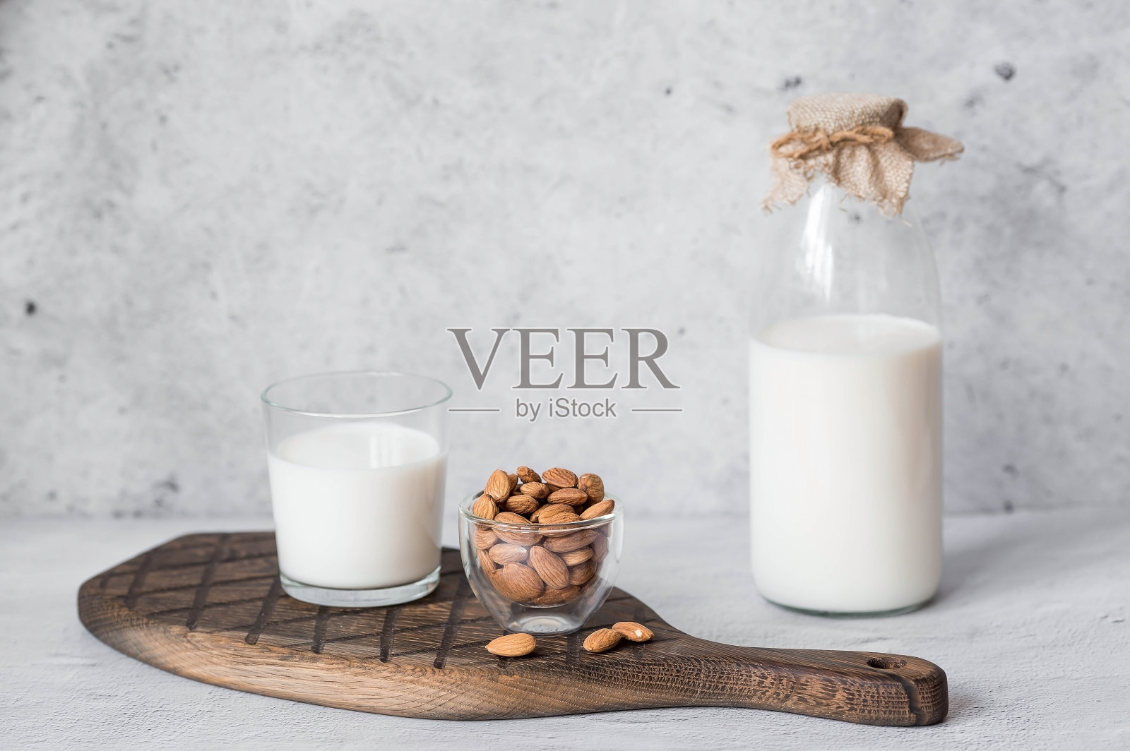 有机杏仁奶装在玻璃瓶里，旁边是放在石桌上的时髦木板上的杏仁。天然环保产品。照片摄影图片