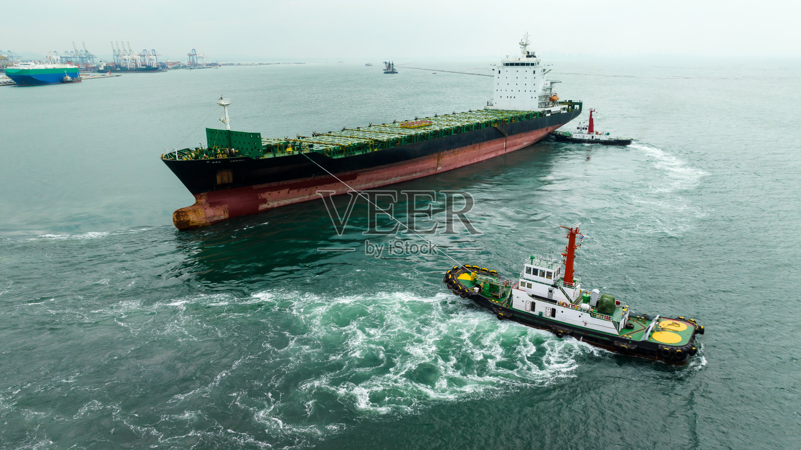 拖船在绿色的海面上拖着货船，照片摄影图片