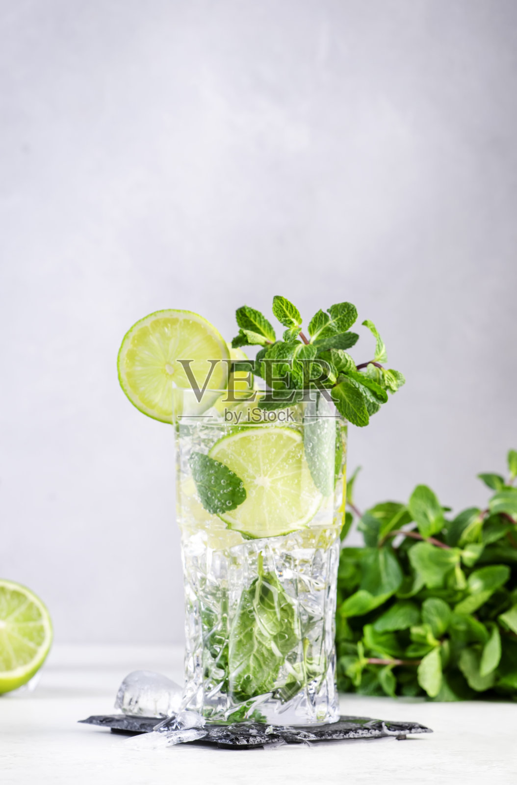 莫吉托夏季酒精鸡尾酒饮料与酸橙，白朗姆酒，苏打水，蔗糖，薄荷和冰在高球杯灰色背景。钢筋工具。本空间照片摄影图片