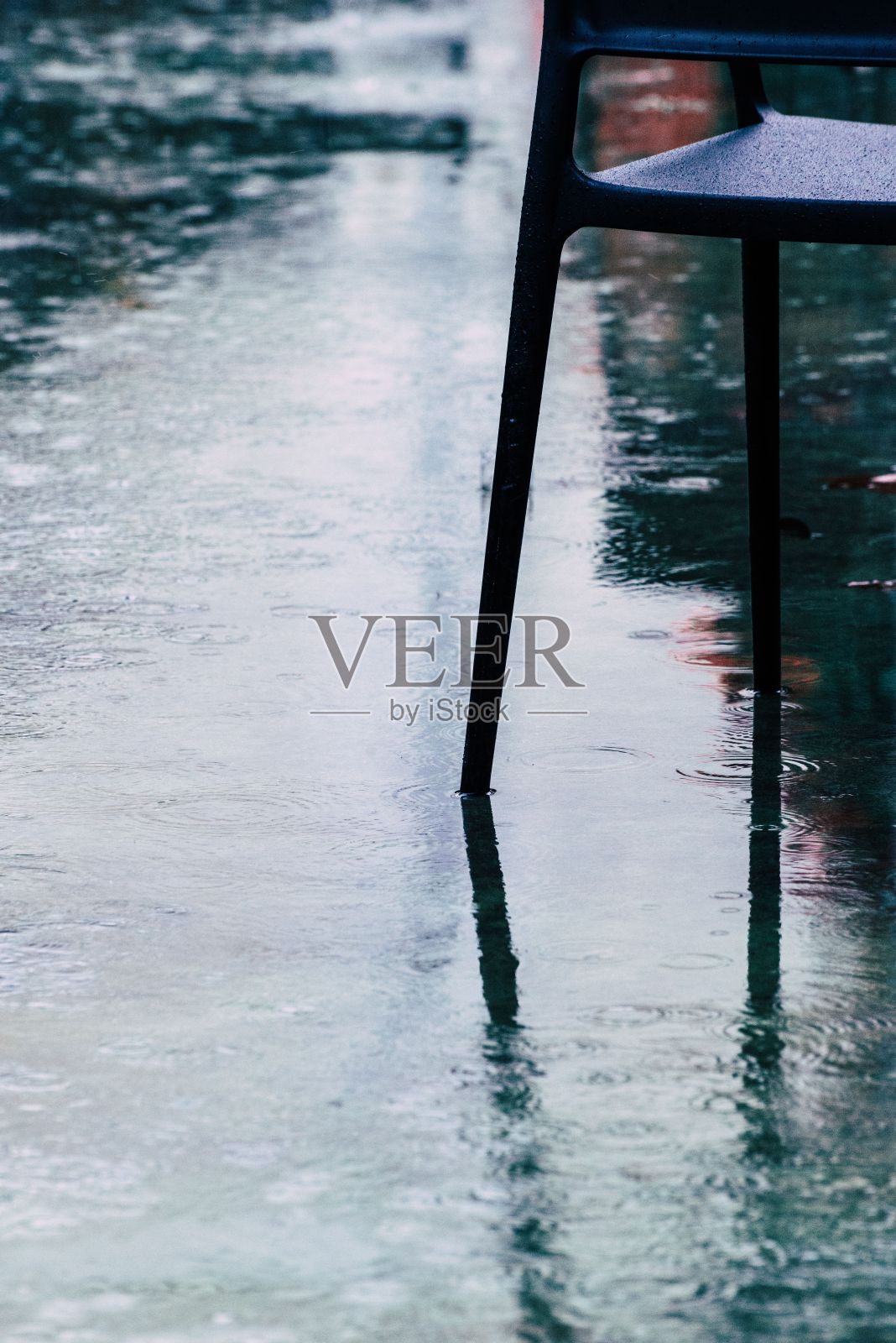 雨中潮湿的人行道旁的金属椅子。照片摄影图片