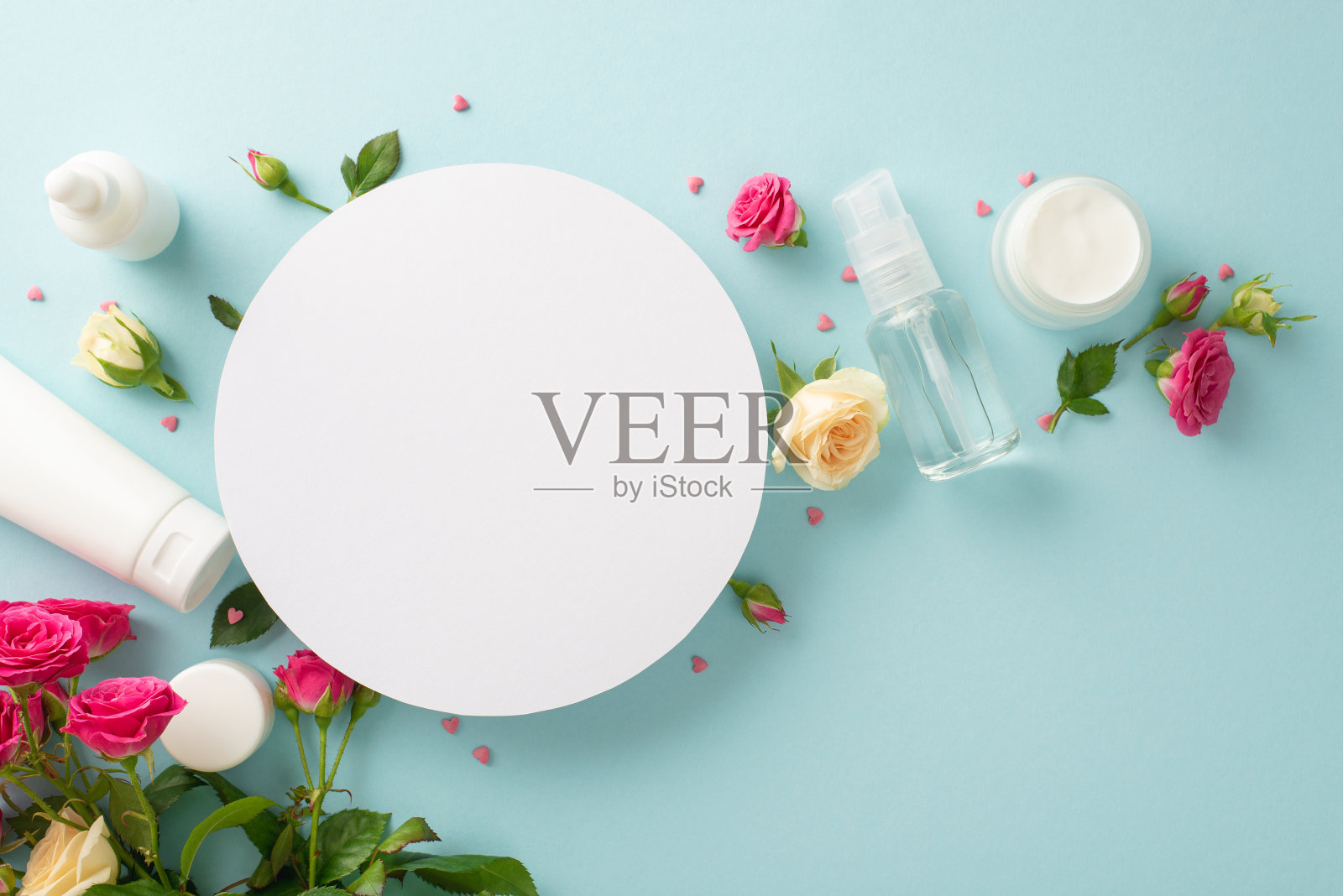 玫瑰疗法概念。护肤产品的俯视图与玫瑰花瓣在柔和的蓝色背景与空白的心脏文字或广告照片摄影图片
