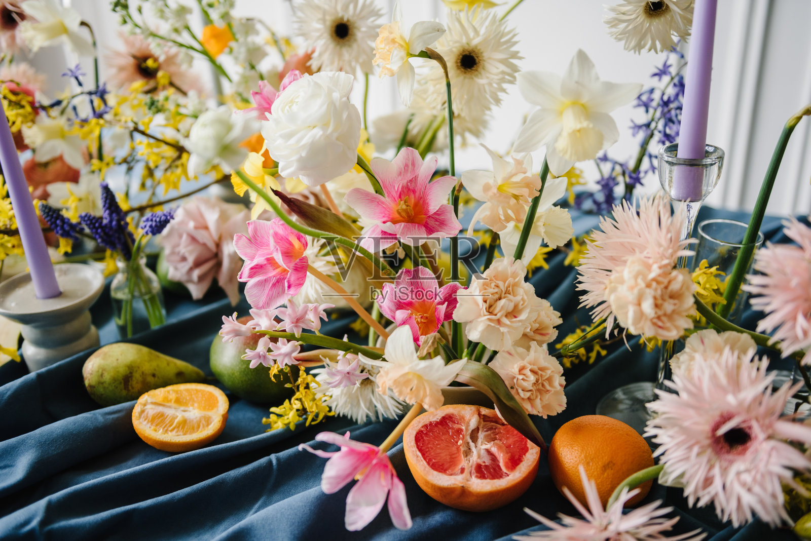 花瓶里有美丽的花束，餐桌上有橘子、梨子、柚子和葡萄柚。家居室内装饰元素。用鲜花、水果、绿色植物、蜡烛装饰节日。夏日花园花的构图照片摄影图片