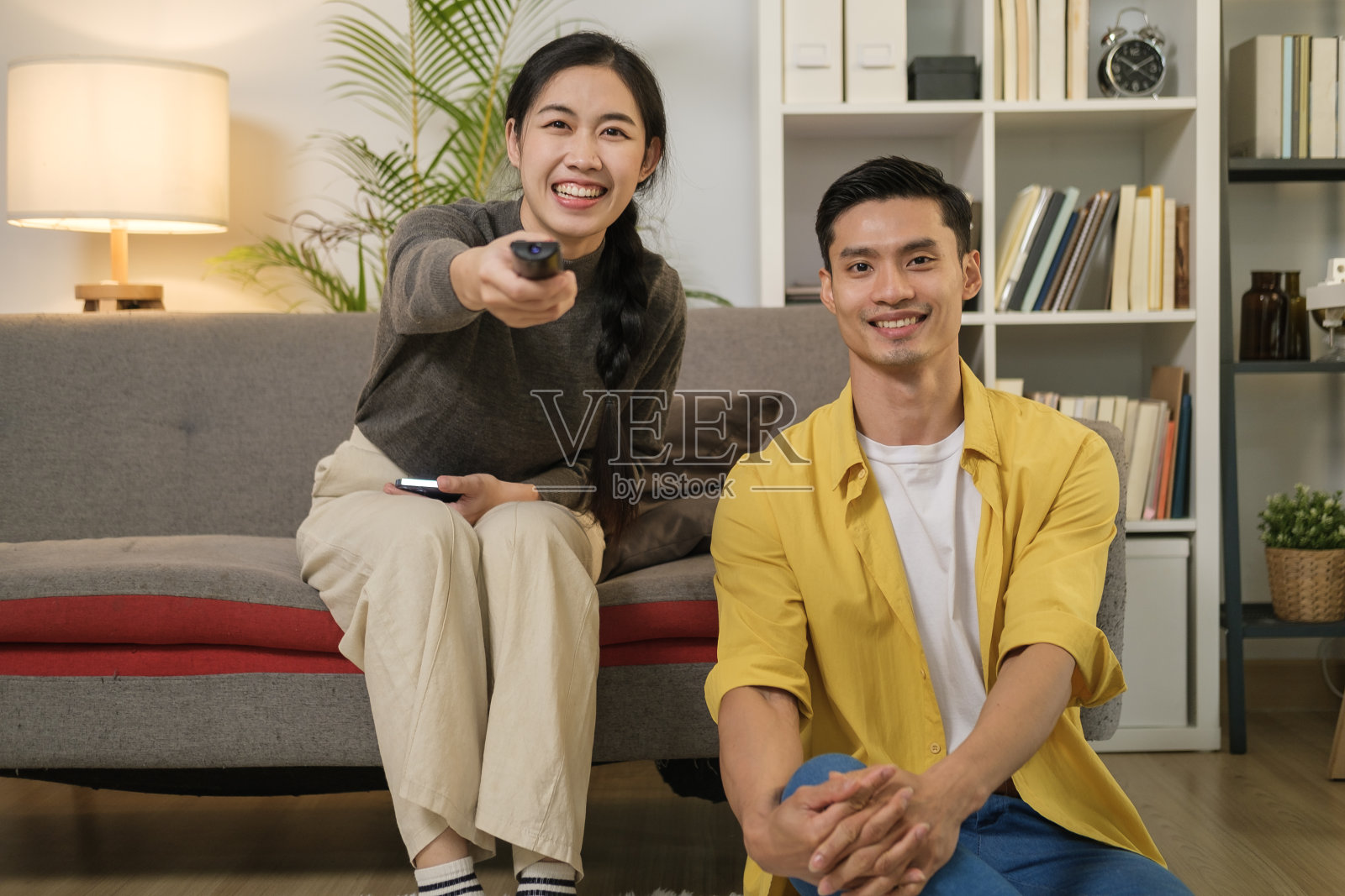 快乐的年轻亚洲夫妇一起看电视在舒适的客厅。人与休闲的理念。照片摄影图片