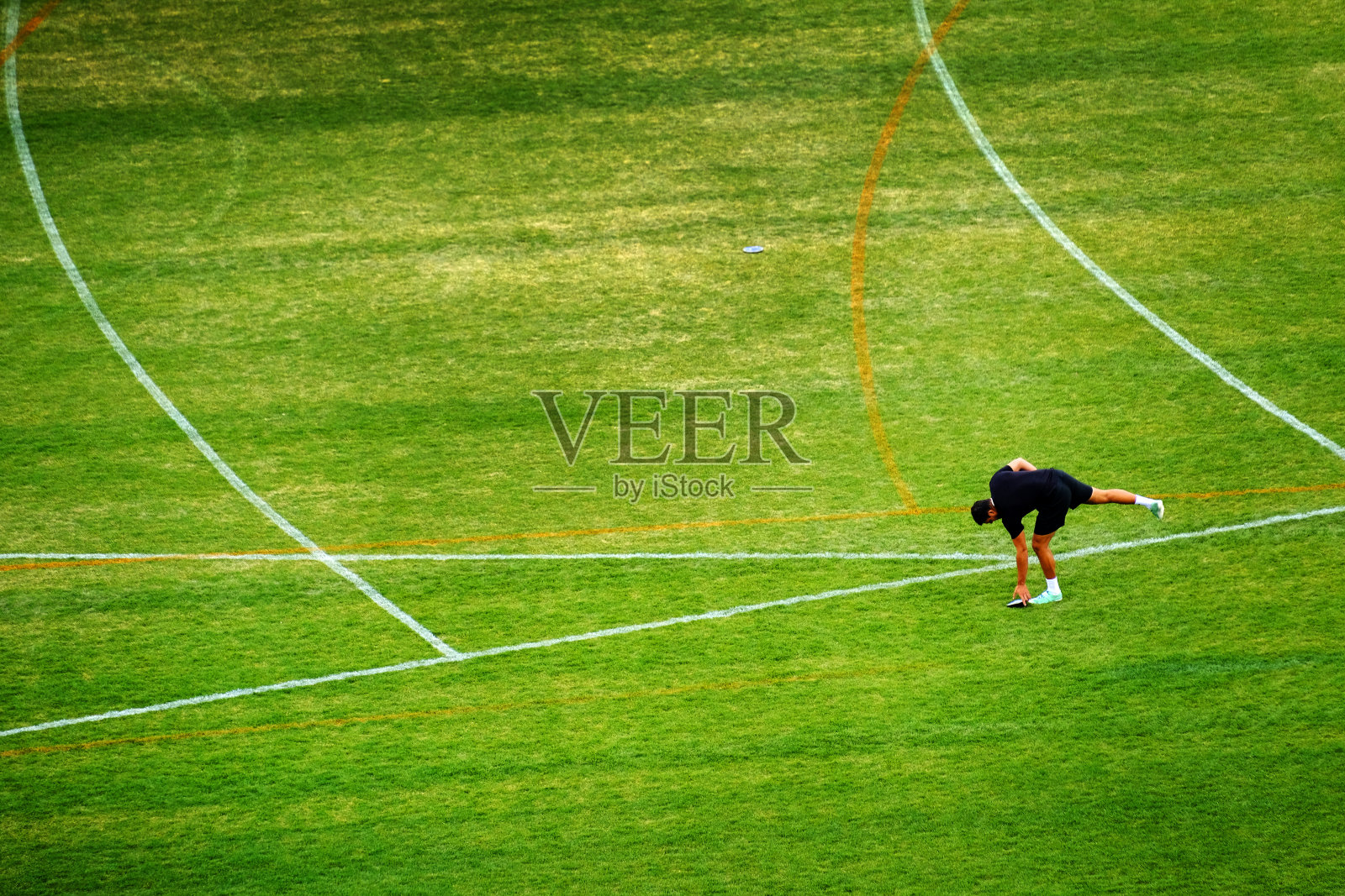 田径运动员掷铁饼后从草地上捡起铁饼照片摄影图片