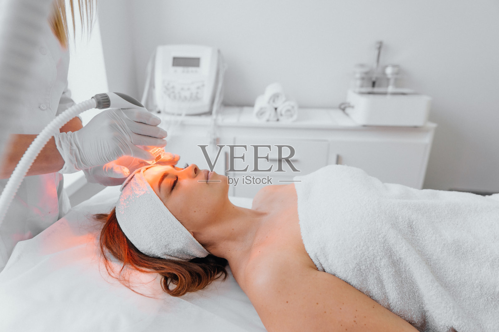 射频整容术。美容师在美容院使用LED设备执行程序。硬件抗老化程序。年轻女子躺着休息放松照片摄影图片