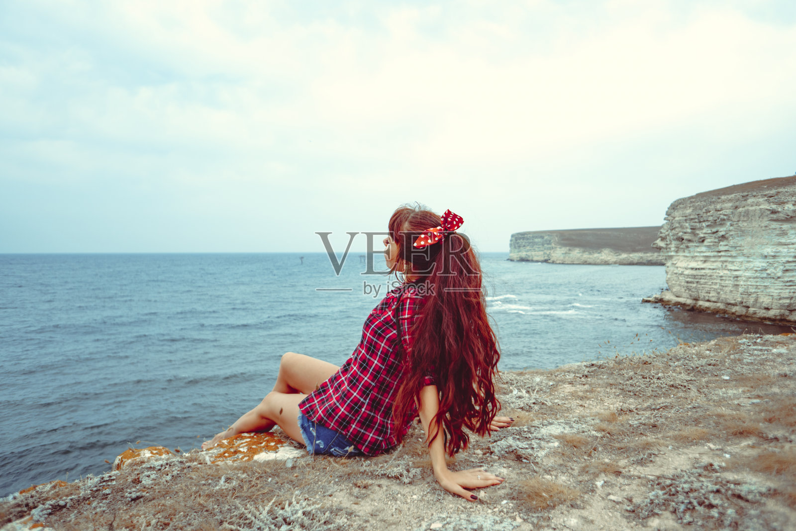 美丽的女孩坐在海边的岩石上照片摄影图片