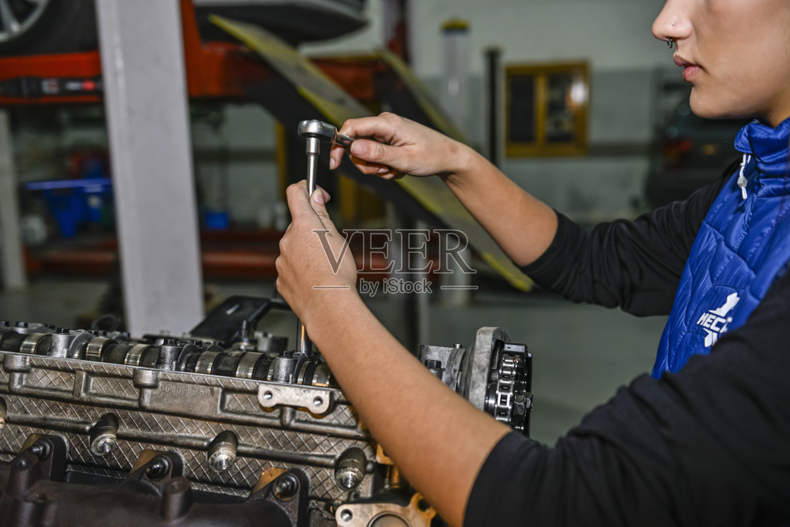 年轻的女机械师，正在修理汽车发动机。照片摄影图片