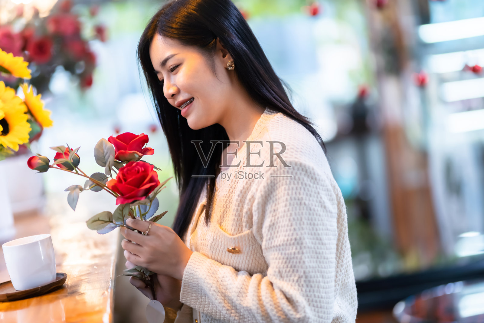情人节，肖像快乐微笑美丽的亚洲年轻女子穿着温暖的衣服拿着一束红玫瑰和玫瑰花瓶在客厅里或咖啡馆里照片摄影图片