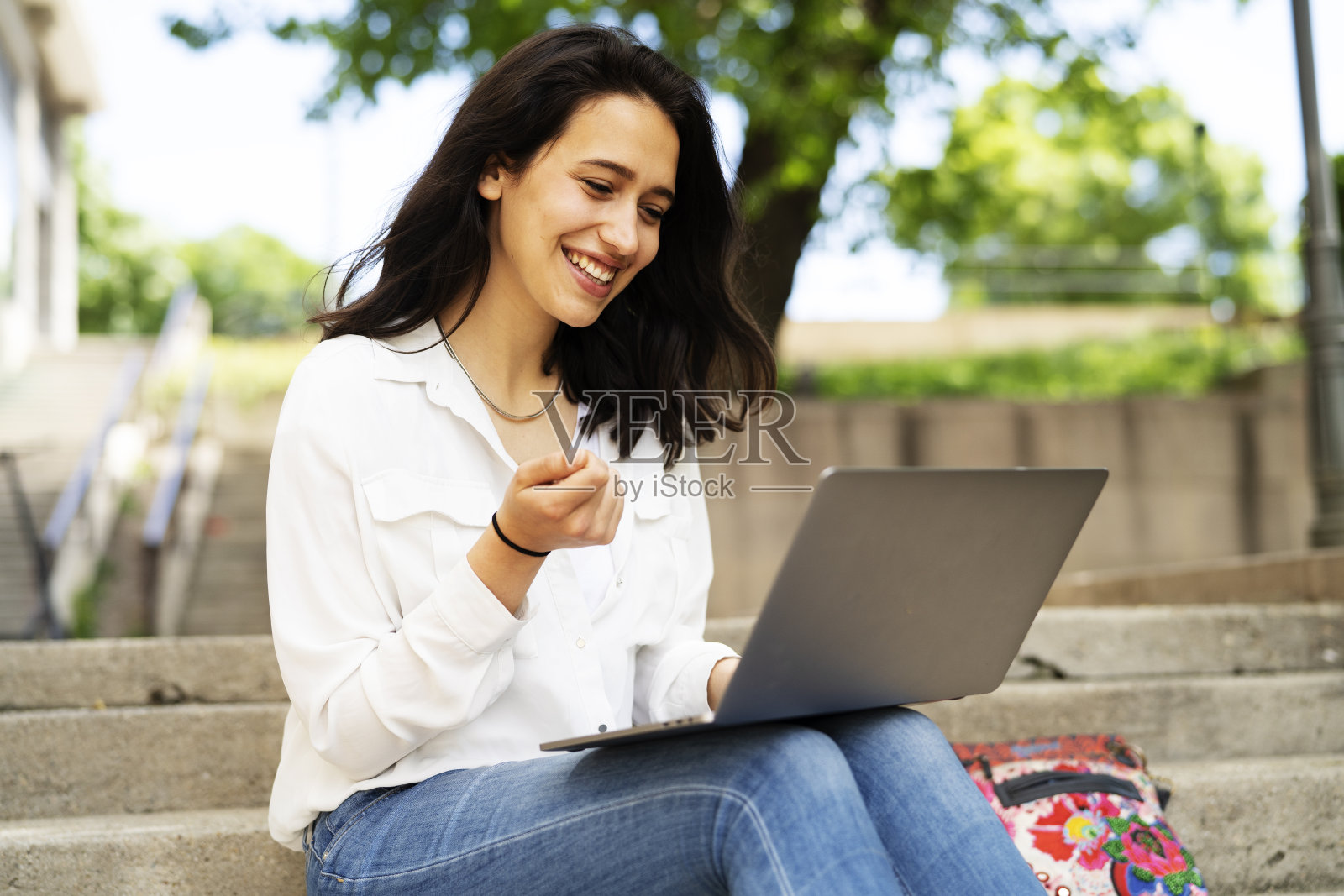 年轻的女商人坐在户外的台阶上，用笔记本电脑工作。照片摄影图片