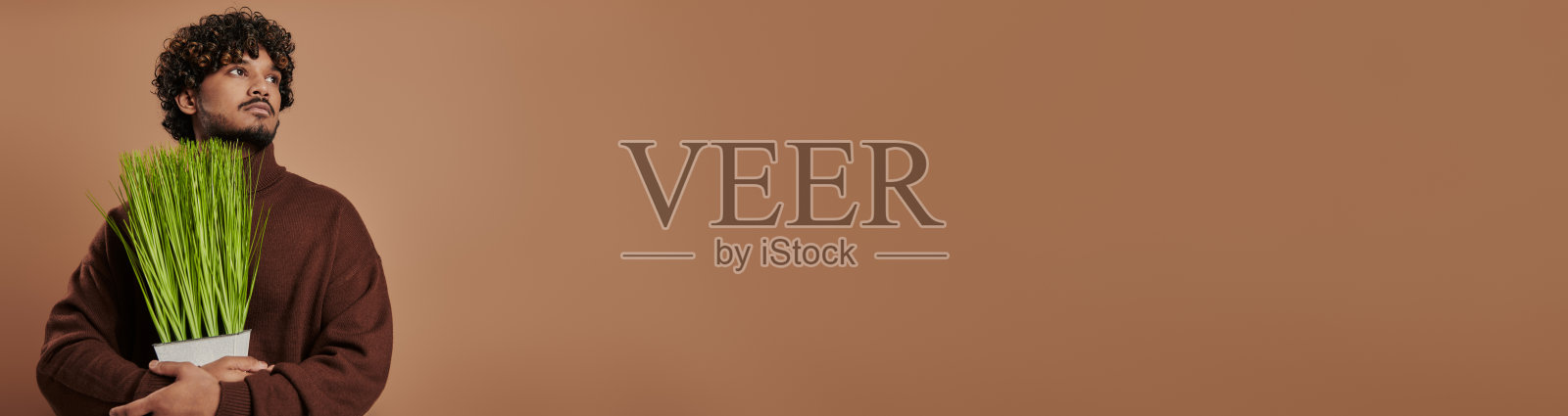 自信的印度男子拿着大麻，棕色背景上是绿草照片摄影图片