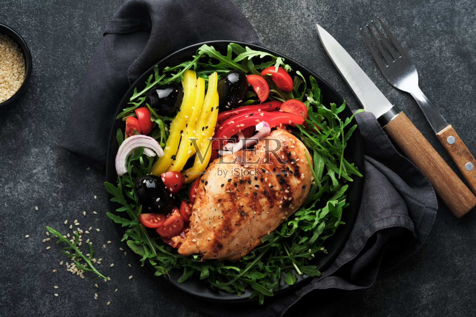 沙拉与烤鸡柳与新鲜芝麻菜，西红柿和橄榄在黑色盘子在旧的深色背景。鸡肉配沙拉。生酮午餐。健康食品。前视图。照片摄影图片