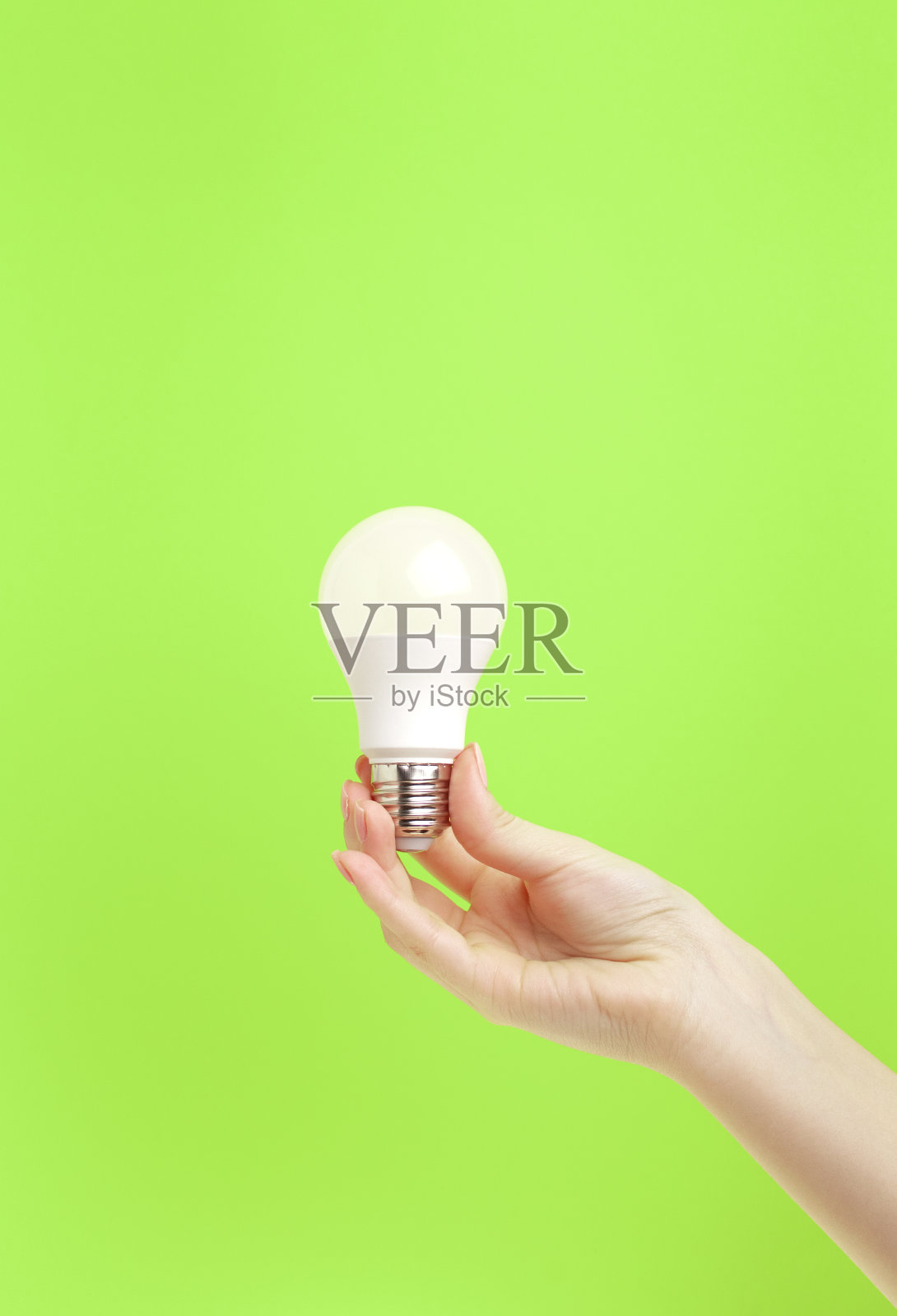 女性手持绿色背景的LED灯。节能理念，替代能源，理念照片摄影图片