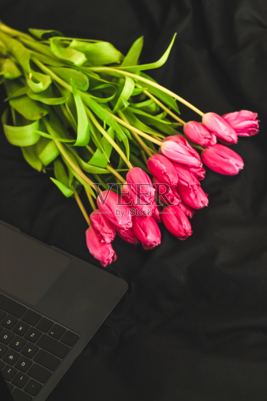黑色时尚亚麻布上的一束粉色花朵和一台打开的笔记本电脑照片摄影图片