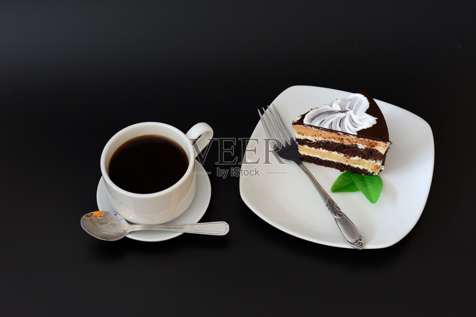 一杯热黑咖啡，用茶托和勺子盛着，盘子里放着一块黑底薄荷巧克力蛋糕。照片摄影图片
