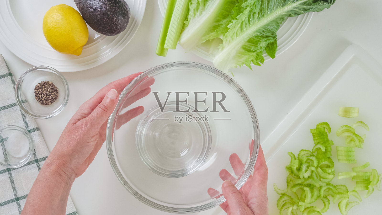 芹菜和生菜沙拉配牛油果，还有柠檬和橄榄油调味配方。食材特写在白色背景上，女子双手，平躺照片摄影图片