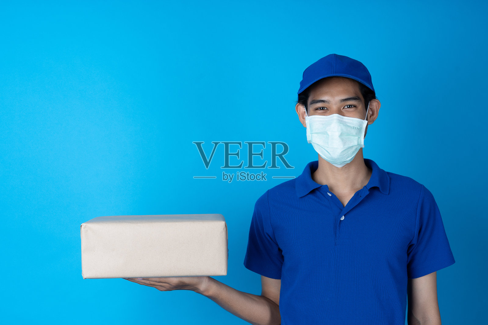 快递员拿着包裹。托运人在货物运输过程中戴上口罩以防止细菌感染。照片摄影图片