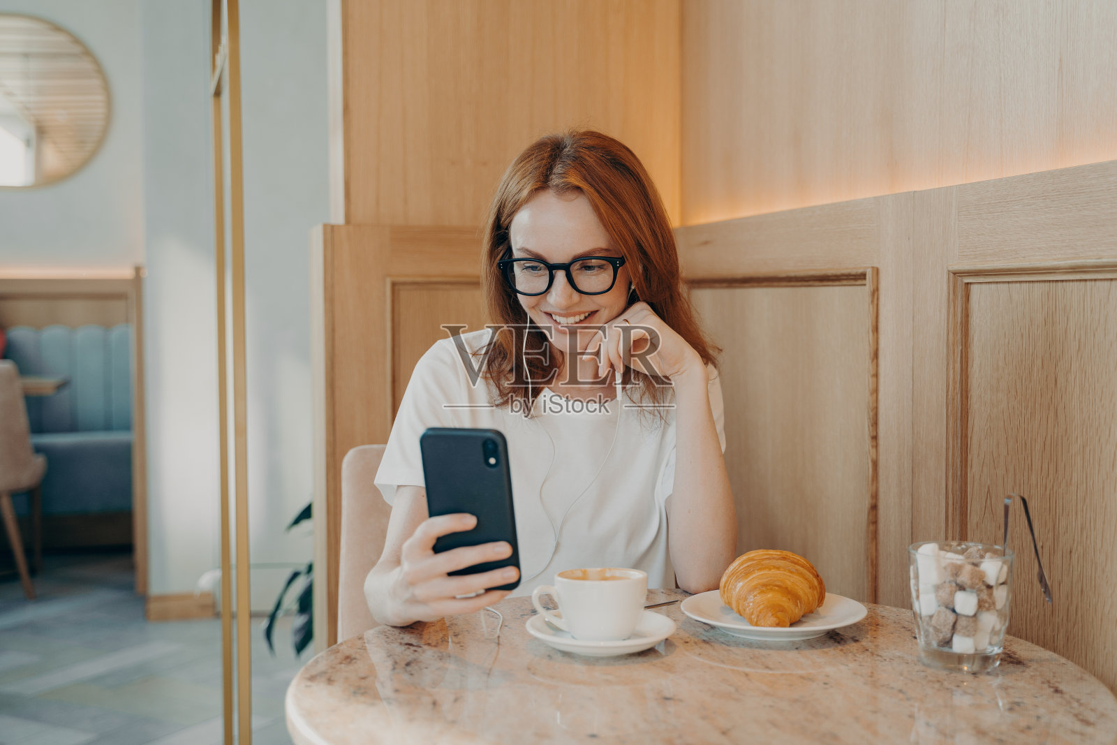 年轻乐观的红发女人戴着耳机坐在咖啡馆里用智能手机上网聊天照片摄影图片