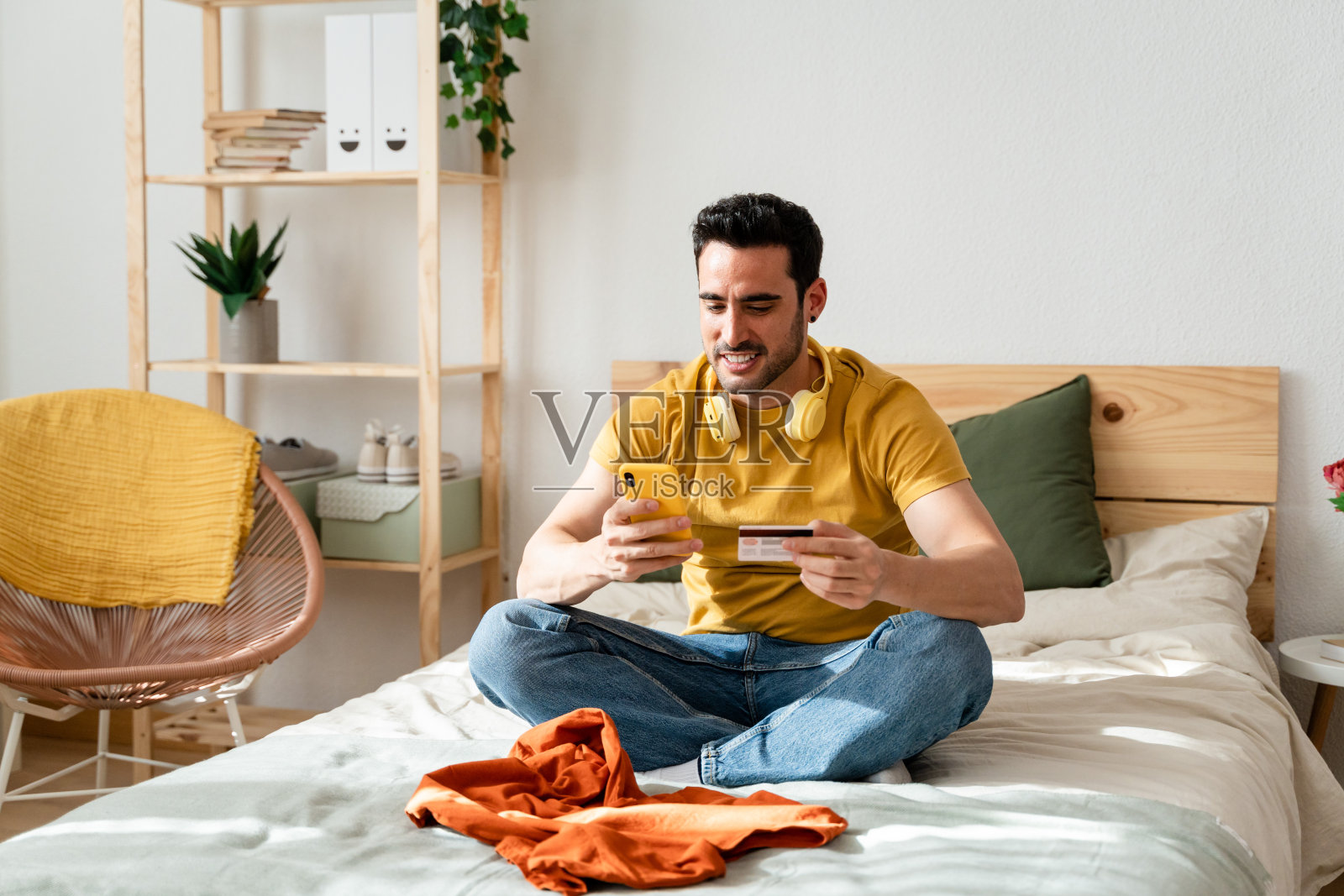 一个男人坐在床上用智能手机网购。照片摄影图片