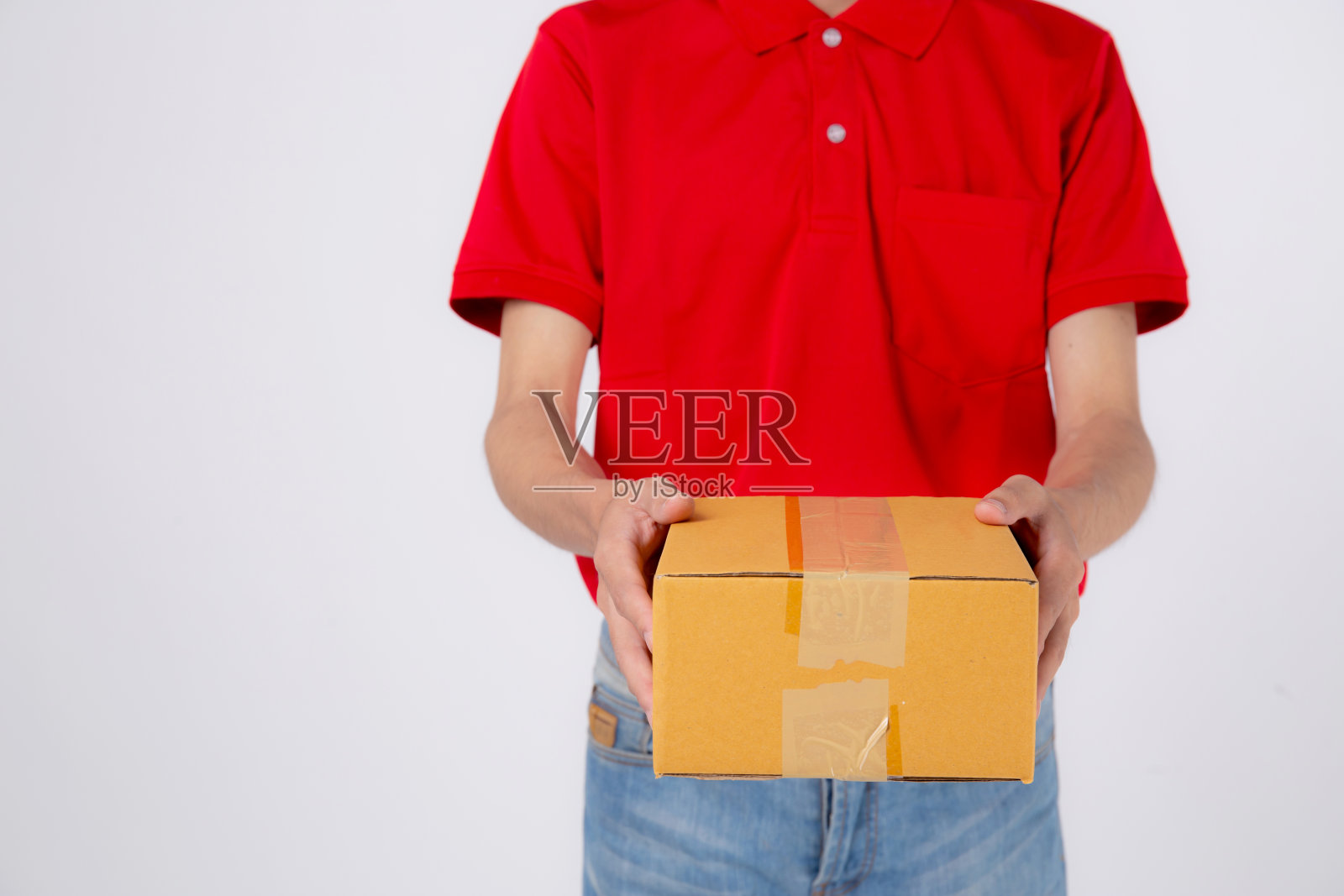 穿着红色制服，戴着帽子的年轻亚洲人站着，拿着孤立的白色背景的箱子堆，员工拿着货物或包裹，快递和派送，运输和服务，物流和货物。照片摄影图片