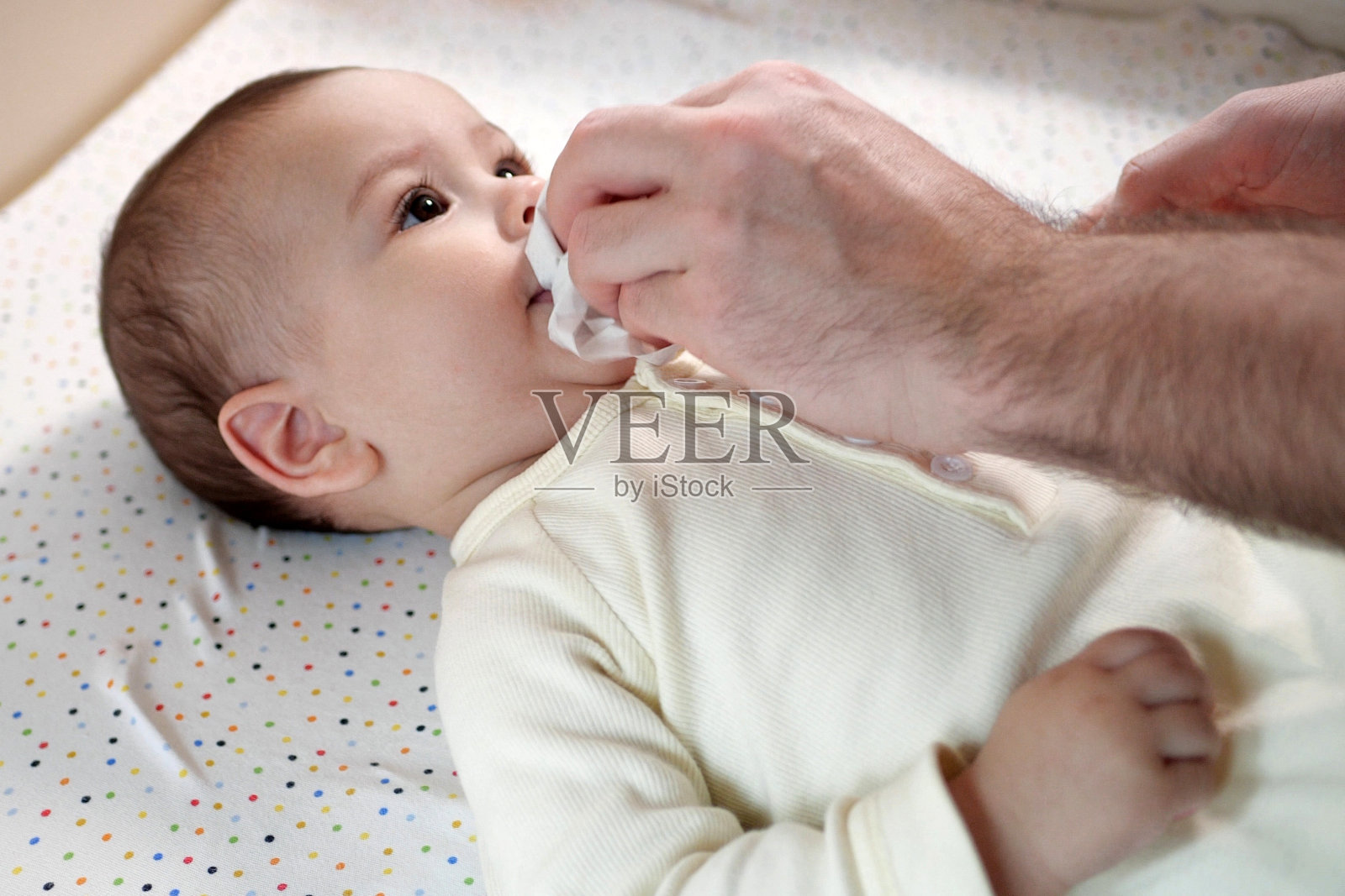 父亲用餐巾擦拭婴儿的嘴，她的小儿子用食物在家里(特写)照片摄影图片