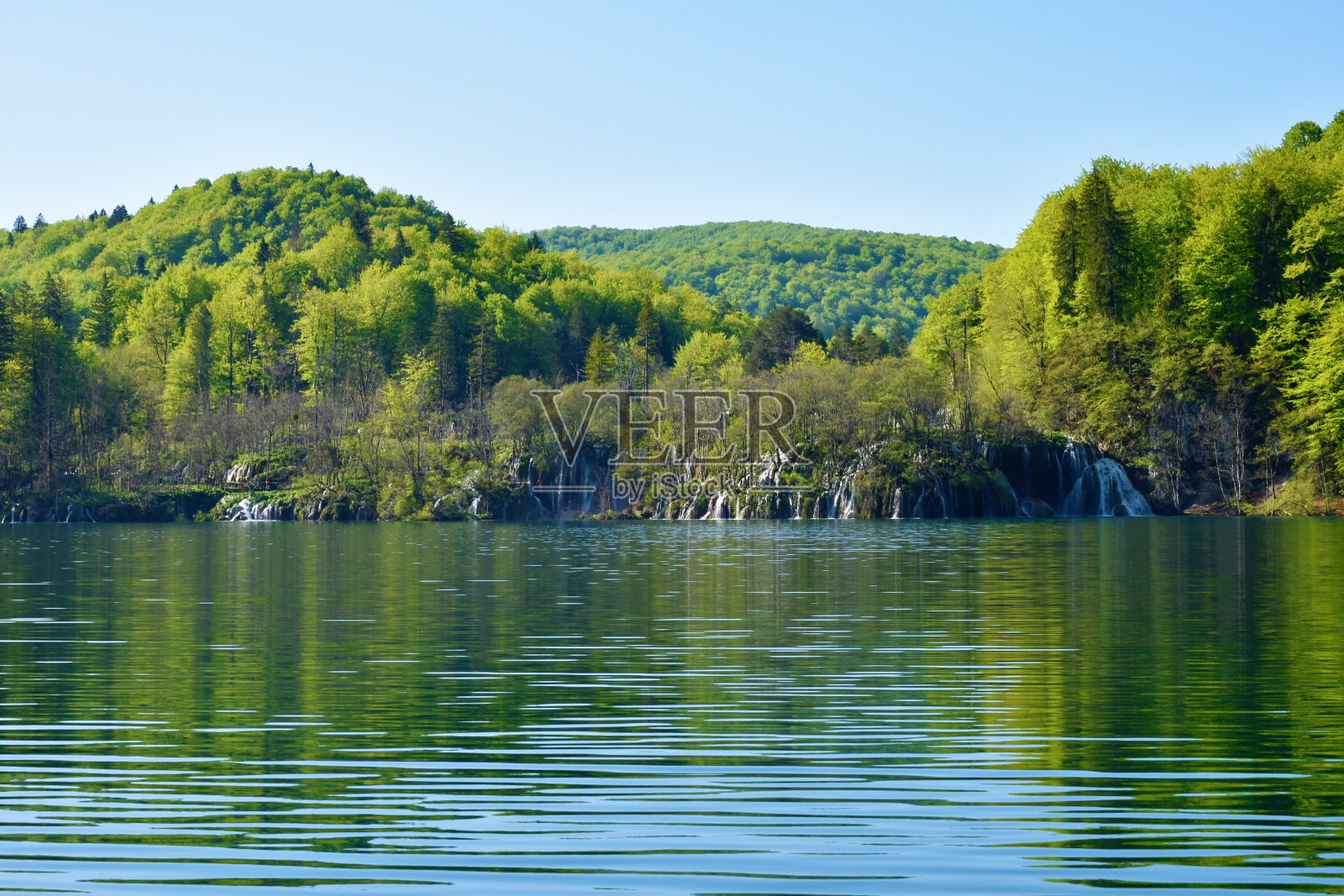 瀑布流入克罗地亚Lika-Senj县Plitvice湖的Kozjak湖，上面是森林覆盖的山丘照片摄影图片