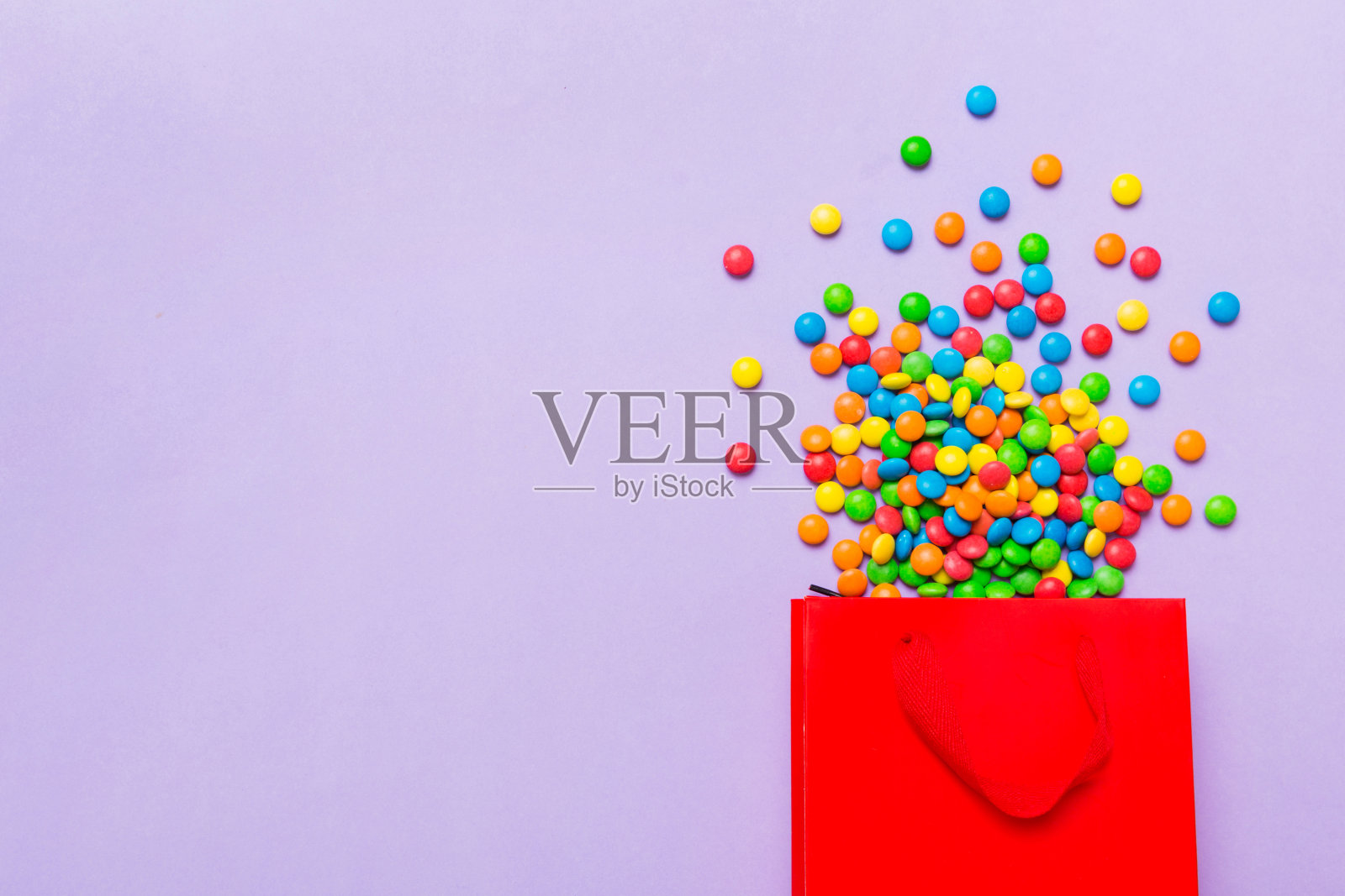 购物纸礼品袋在角落里充满了各种传统糖果落在彩色背景与复制空间。快乐假期销售概念照片摄影图片