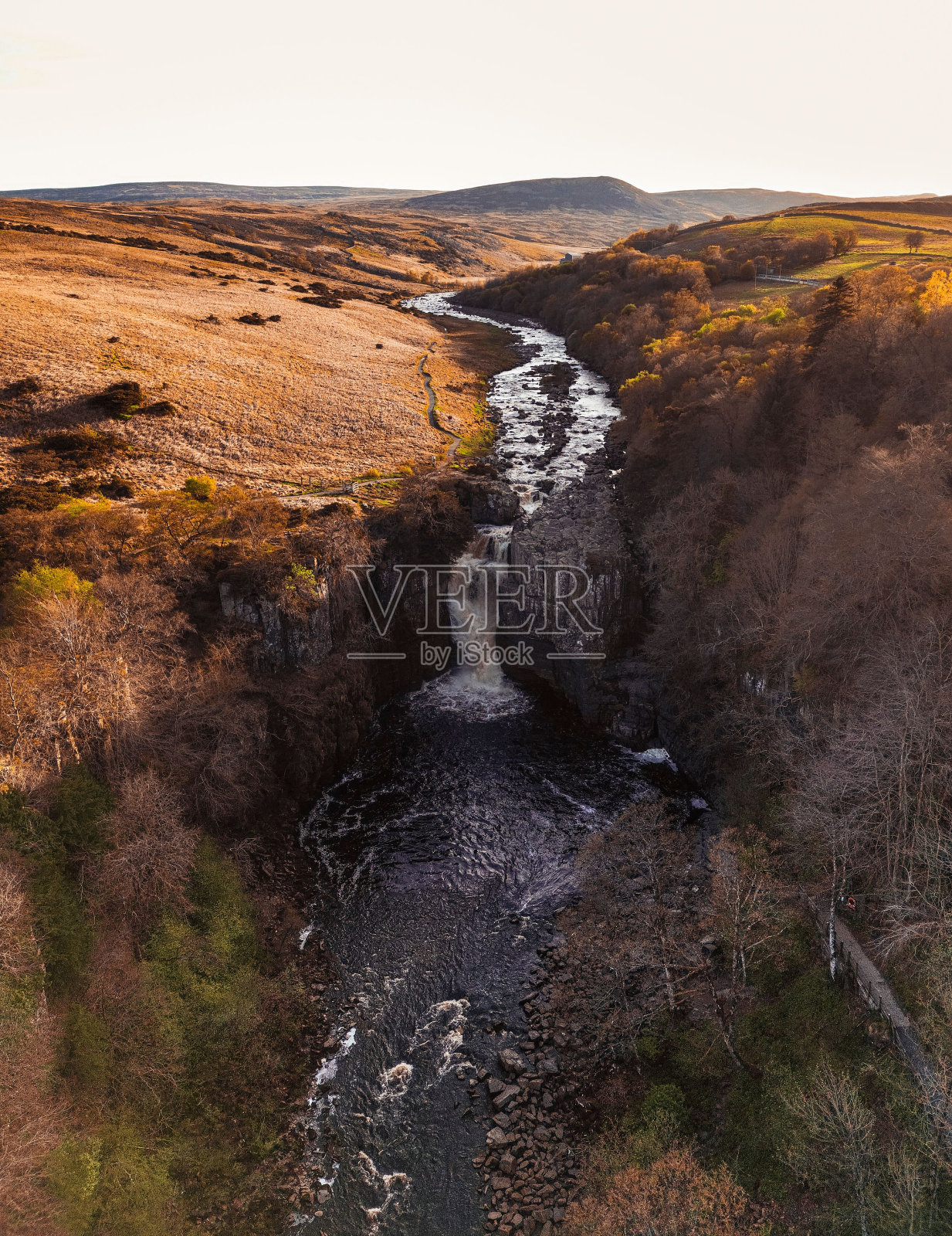 雄伟的瀑布在茂密的树木和开阔的田野之间穿过岩石地形照片摄影图片