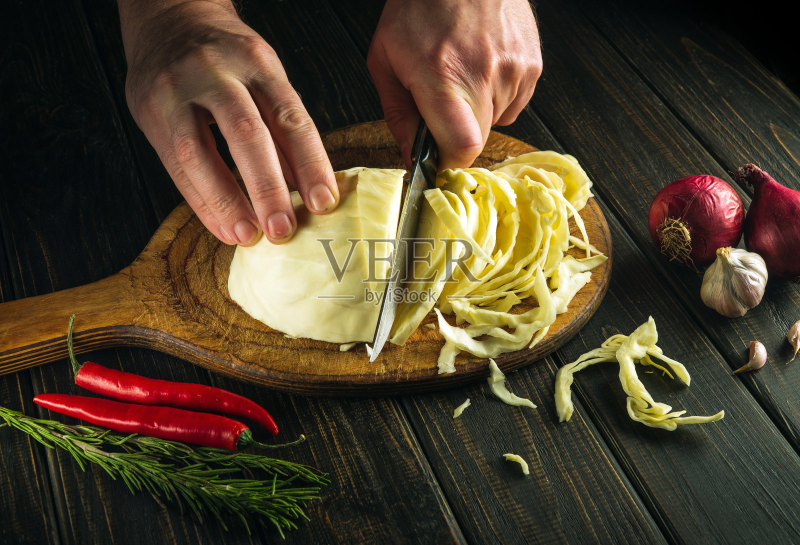 厨师的双手用刀切开新鲜的卷心菜，准备在餐厅的厨房桌子上做一道菜。蔬菜饮食的想法。照片摄影图片