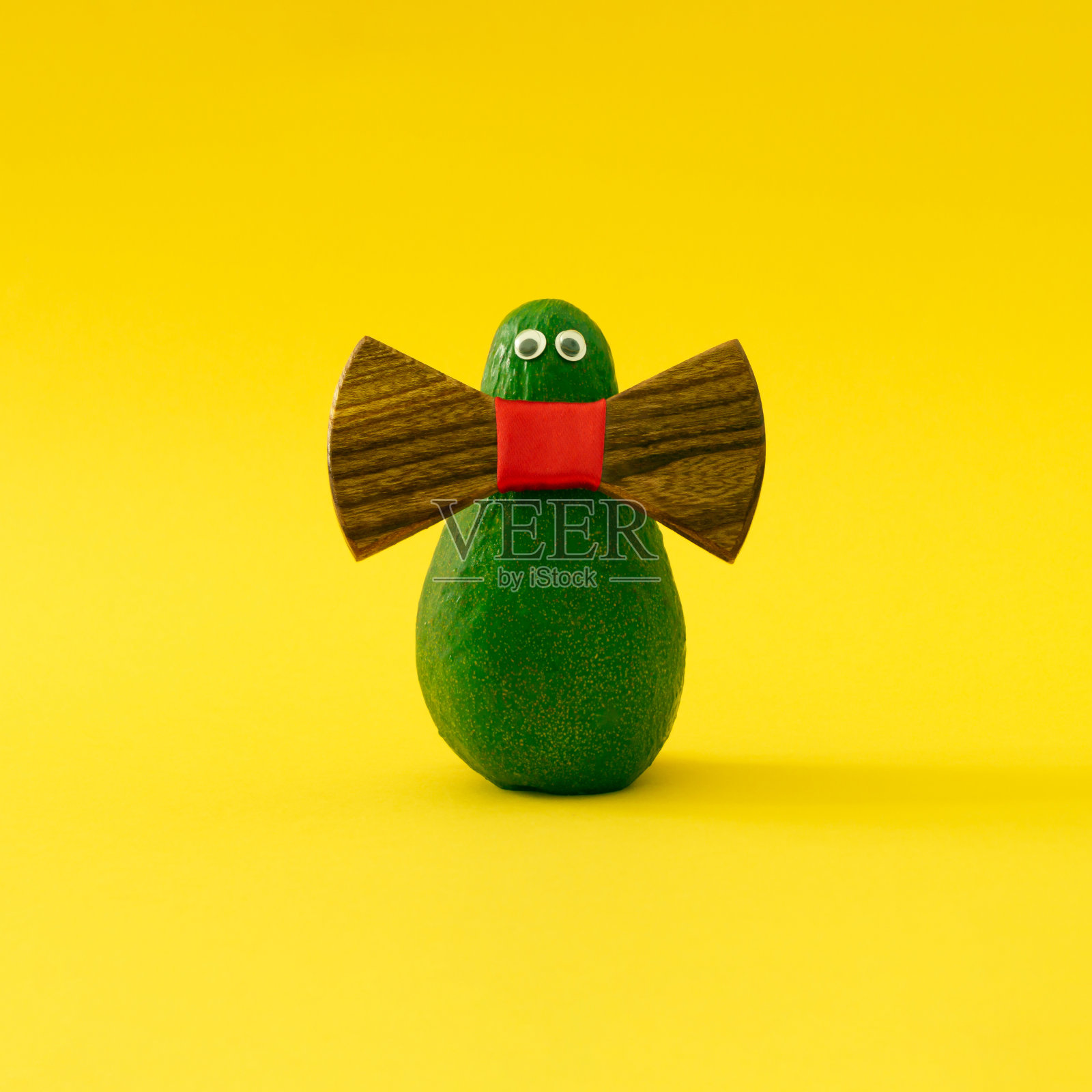 时髦的鳄梨先生。有趣的最小概念制成的新鲜牛油果在浅黄色的背景。自然时尚设计。照片摄影图片