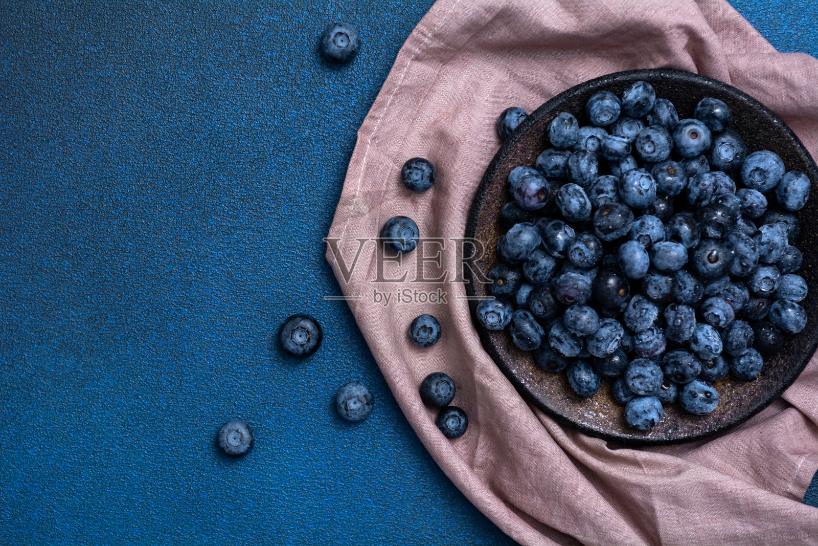盘子里有蓝色背景的新鲜蓝莓。有新鲜浆果的餐巾。从上面看。专注于餐盘照片摄影图片