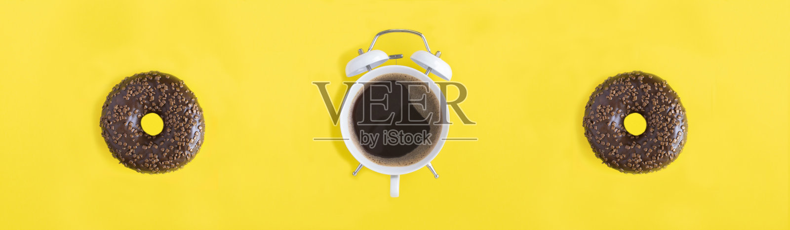 白色闹钟表盘上的黑咖啡和黄色背景上的巧克力釉甜甜圈。前视图。照片摄影图片