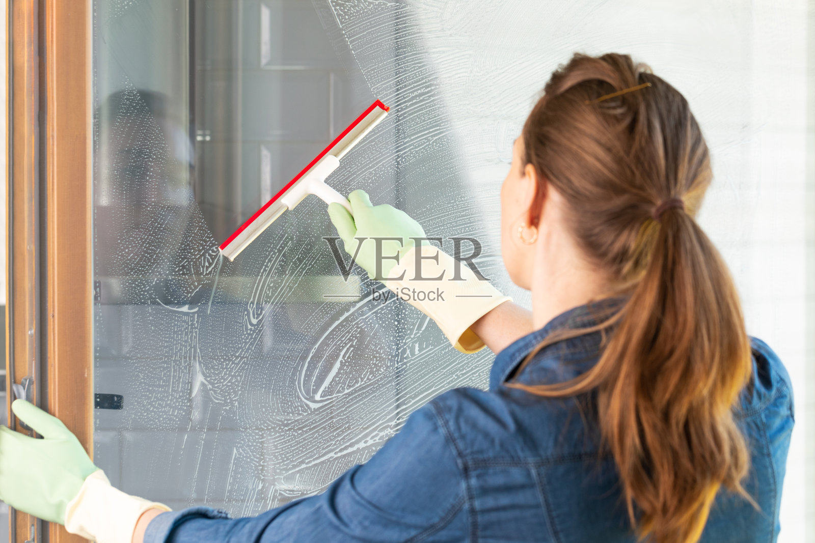 在阳光明媚的温暖日子里用橡胶刮刀对窗户进行春季清洁。干净和新鲜的房子。照片摄影图片