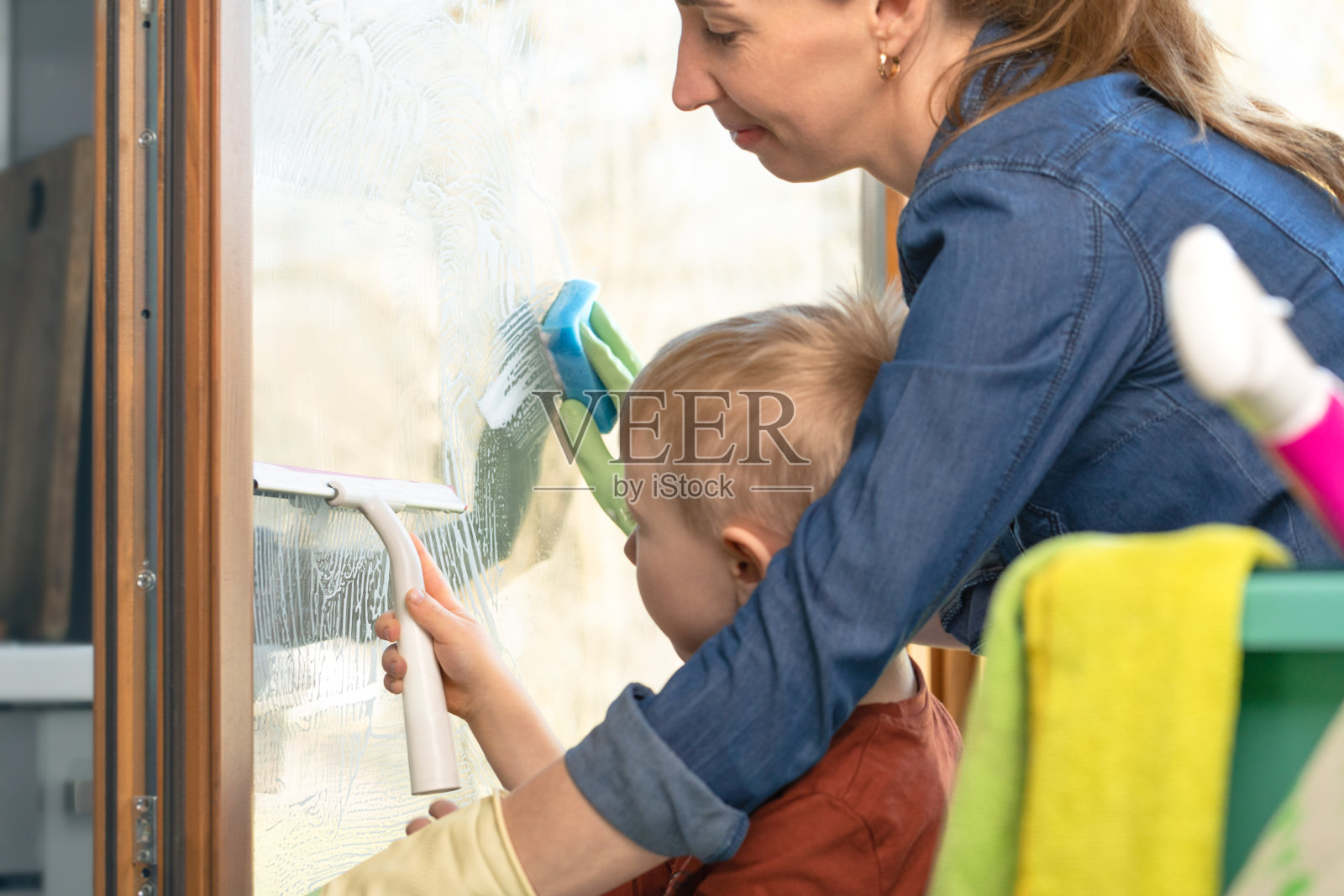 在阳光明媚的温暖日子里用橡胶刮刀对窗户进行春季清洁。干净和新鲜的房子。妇女和儿童的家庭作业照片摄影图片