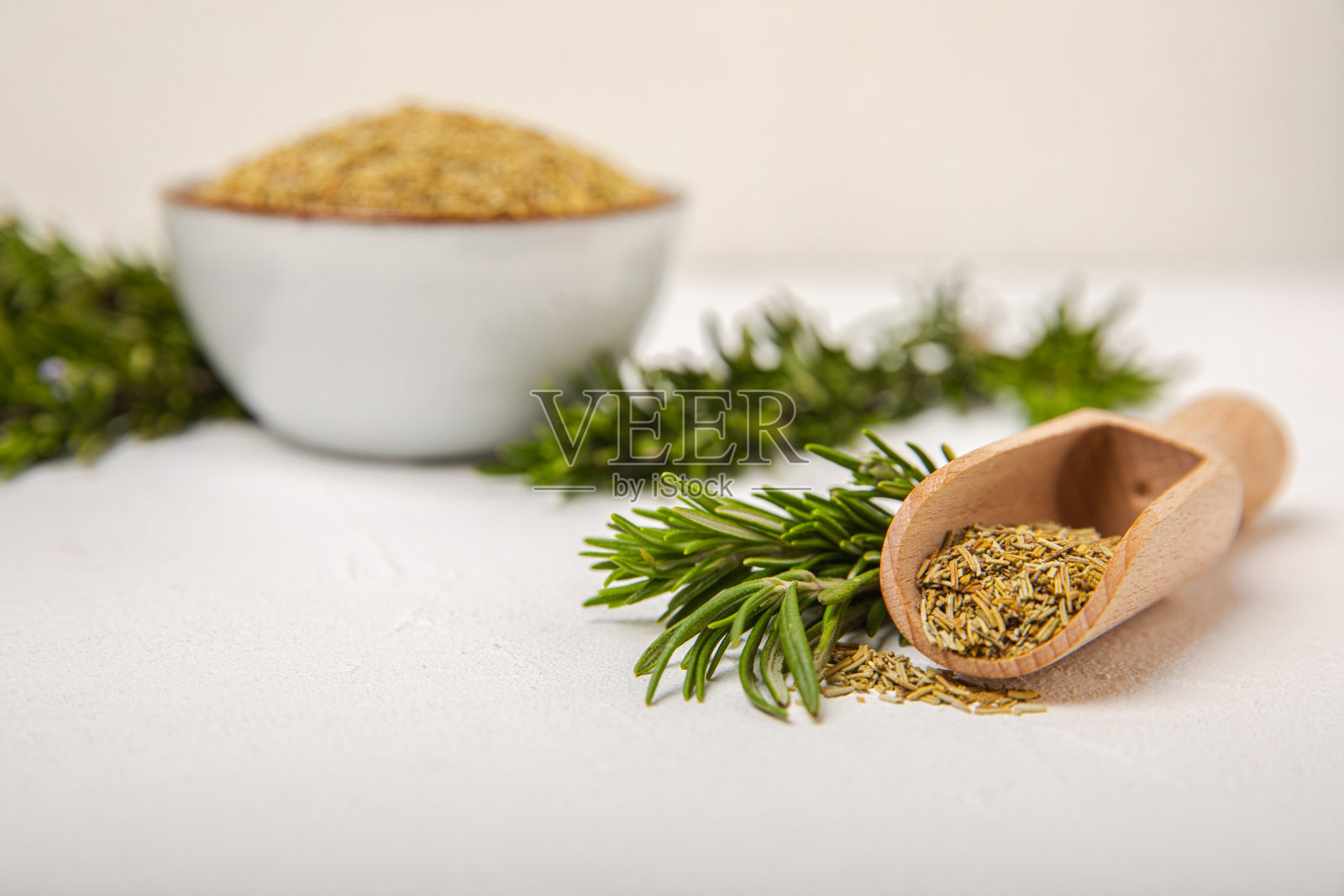 干迷迭香放在玻璃罐里和木勺里，新鲜迷迭香的枝条在白色纹理的背景上。用于肉和鱼的香料和香草。食谱。烹饪概念。有机草本植物。放文字的地方。照片摄影图片