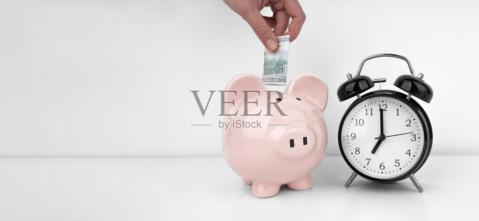 女人的手把美元钞票放进一个带闹钟的储蓄罐照片摄影图片