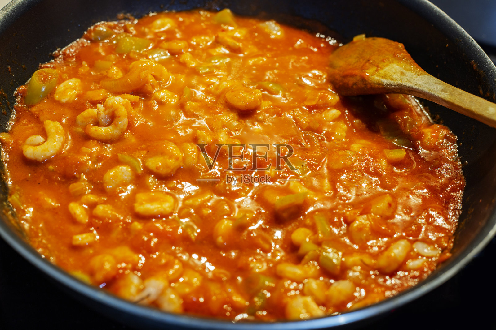 用木勺在黑锅里用番茄酱煮蔬菜虾仁照片摄影图片