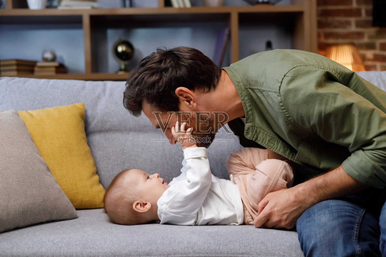 爸爸在舒适公寓的沙发上和他的小宝贝玩耍。父爱。父亲拥抱并亲吻他的小女儿。照片摄影图片