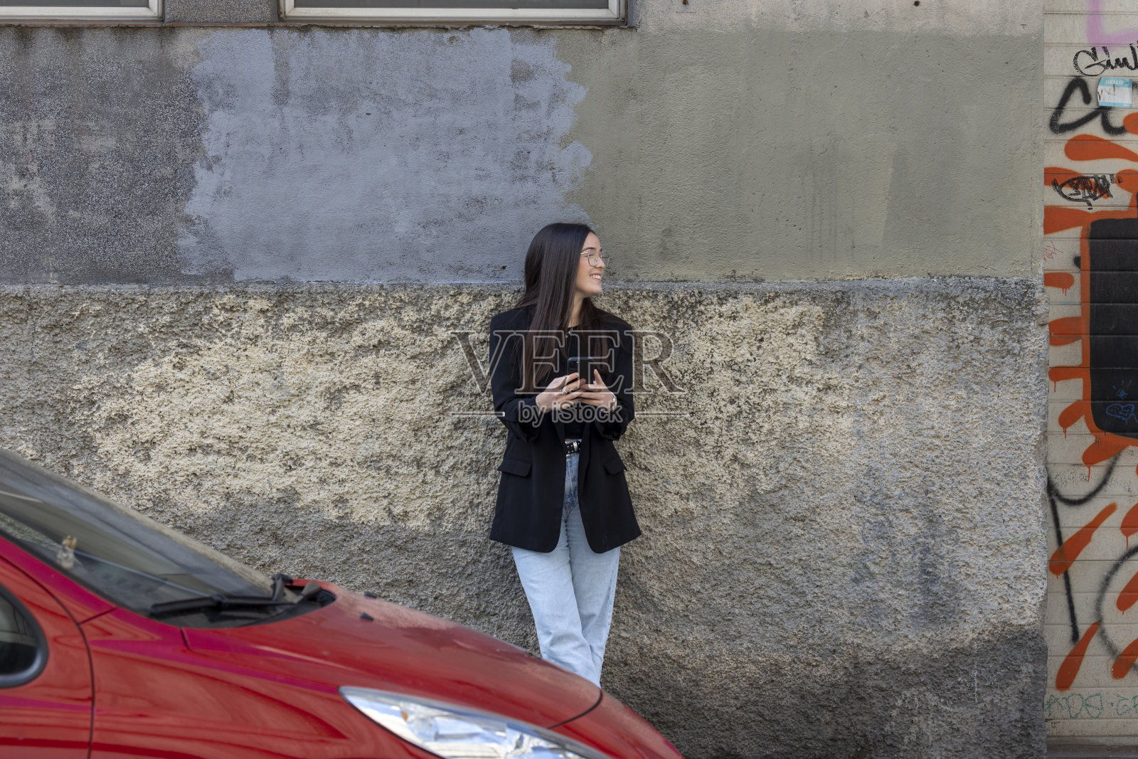 年轻女子在巴塞罗那的城市中使用她的手机，前方是一辆红色的汽车照片摄影图片