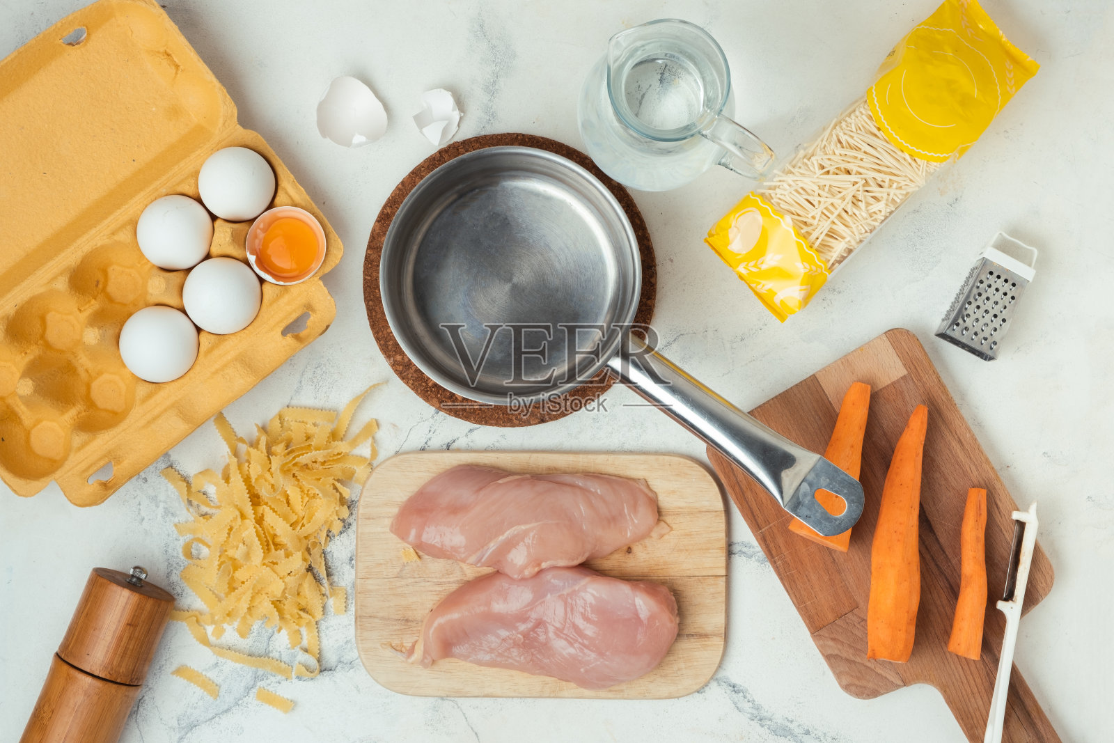 白色大理石背景上的汤料平面。鸡汤的烹饪过程。肉、意大利面、蔬菜都可以在金属锅里煮了。俯视图照片摄影图片