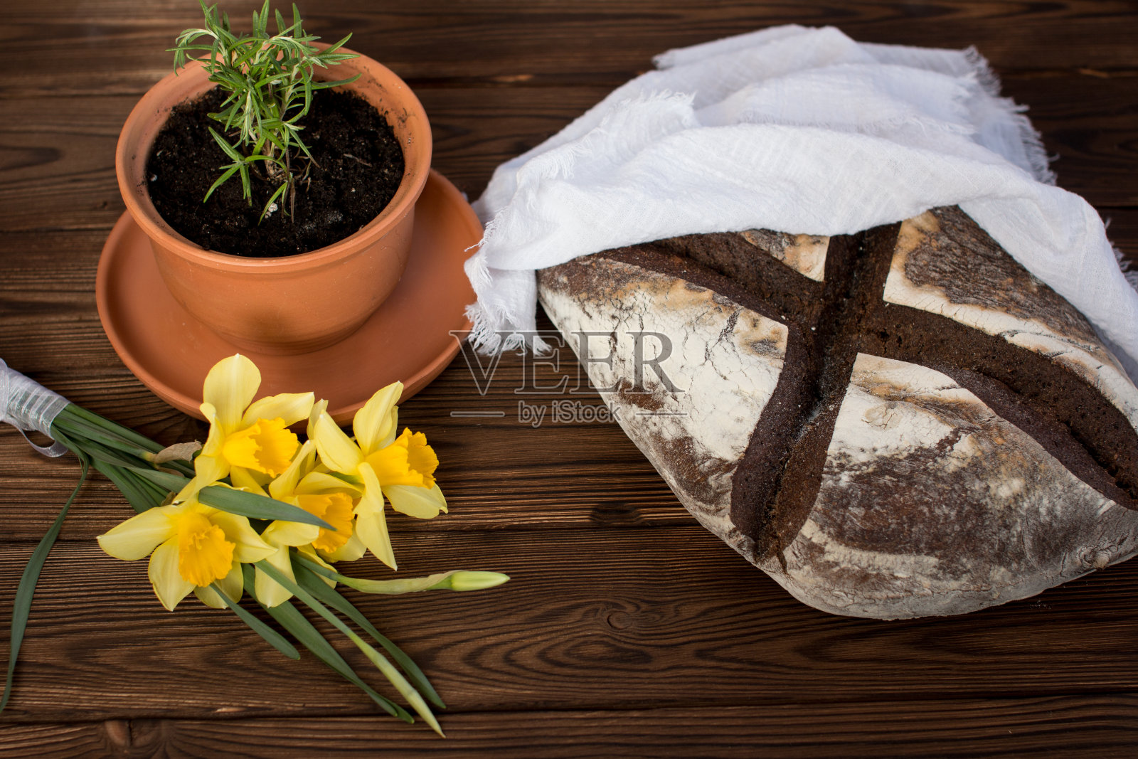 质朴的桌子上放着刚烤好的黑面包。一束水仙花，黄色的花照片摄影图片