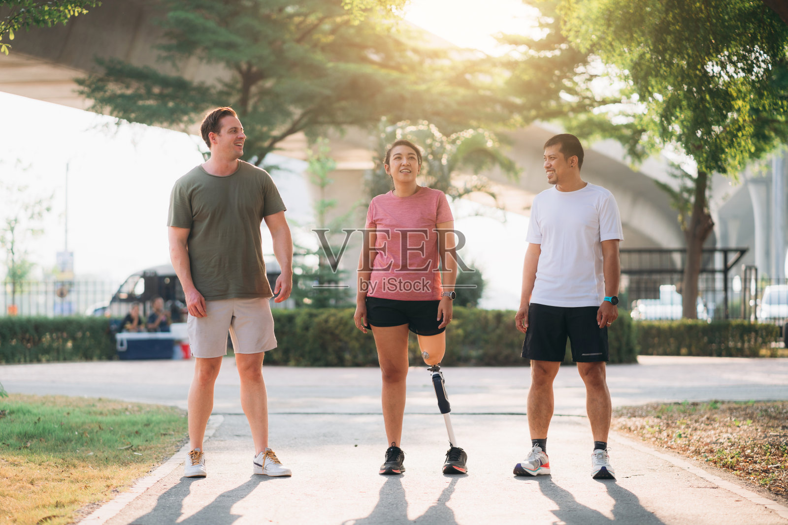 一名女子在公园里锻炼，她的朋友帮她支撑着她的义肢。人们肩并肩在公园外慢跑。女性在户外散步和锻炼。照片摄影图片